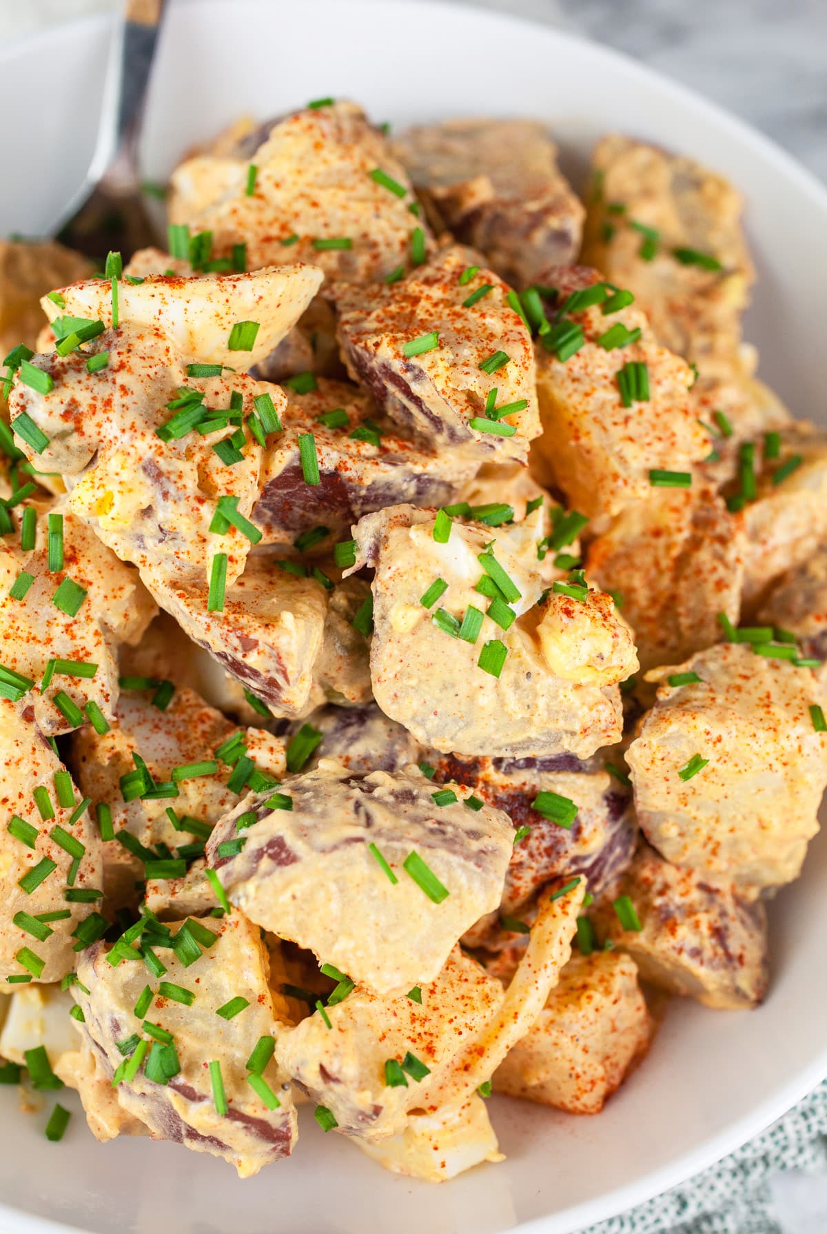 Spanish potato salad with minced chives in white bowl.