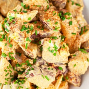 Spanish style potato salad with chives in white bowl.