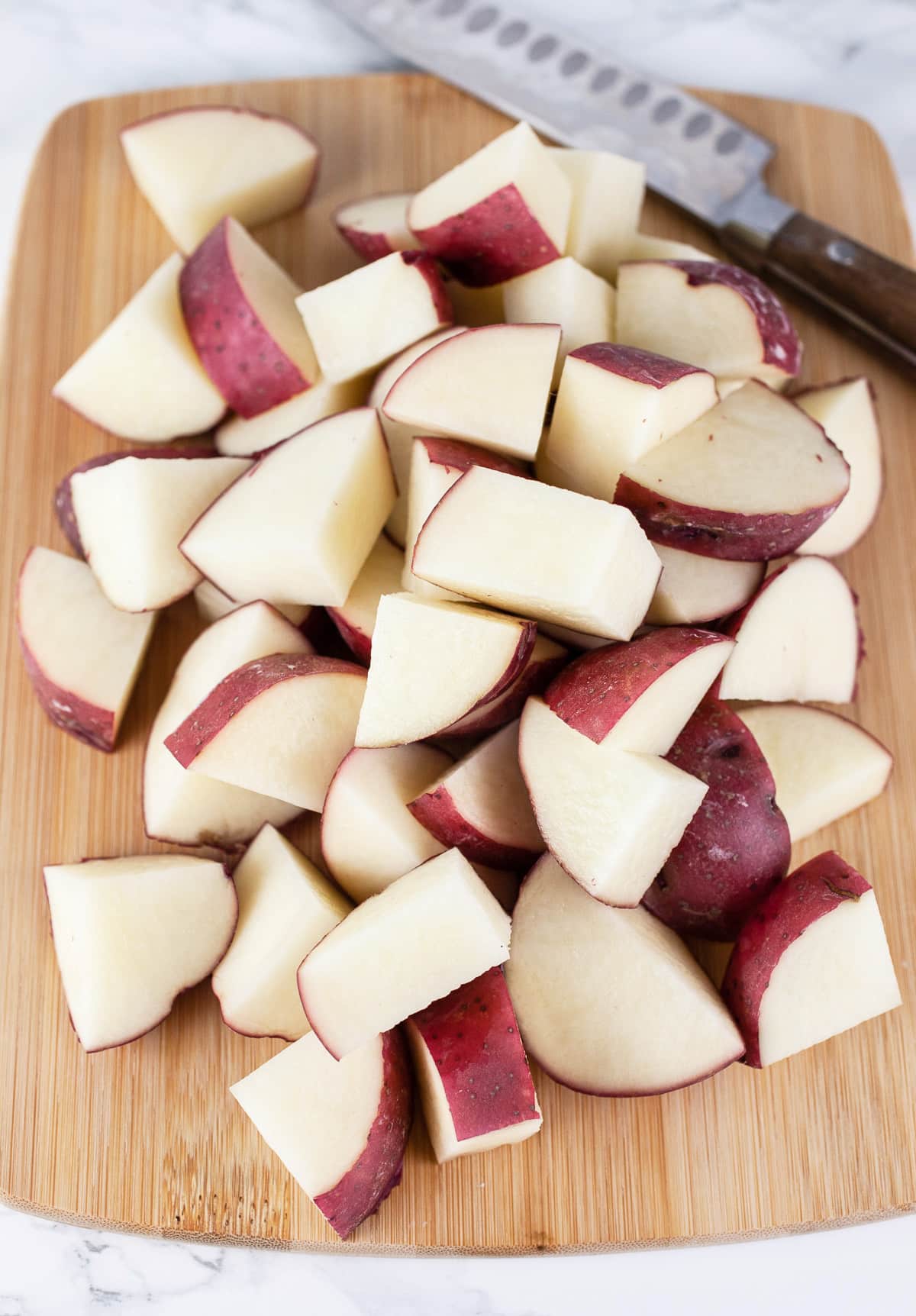 Diced red potatoes on wooden cutting board with knife.