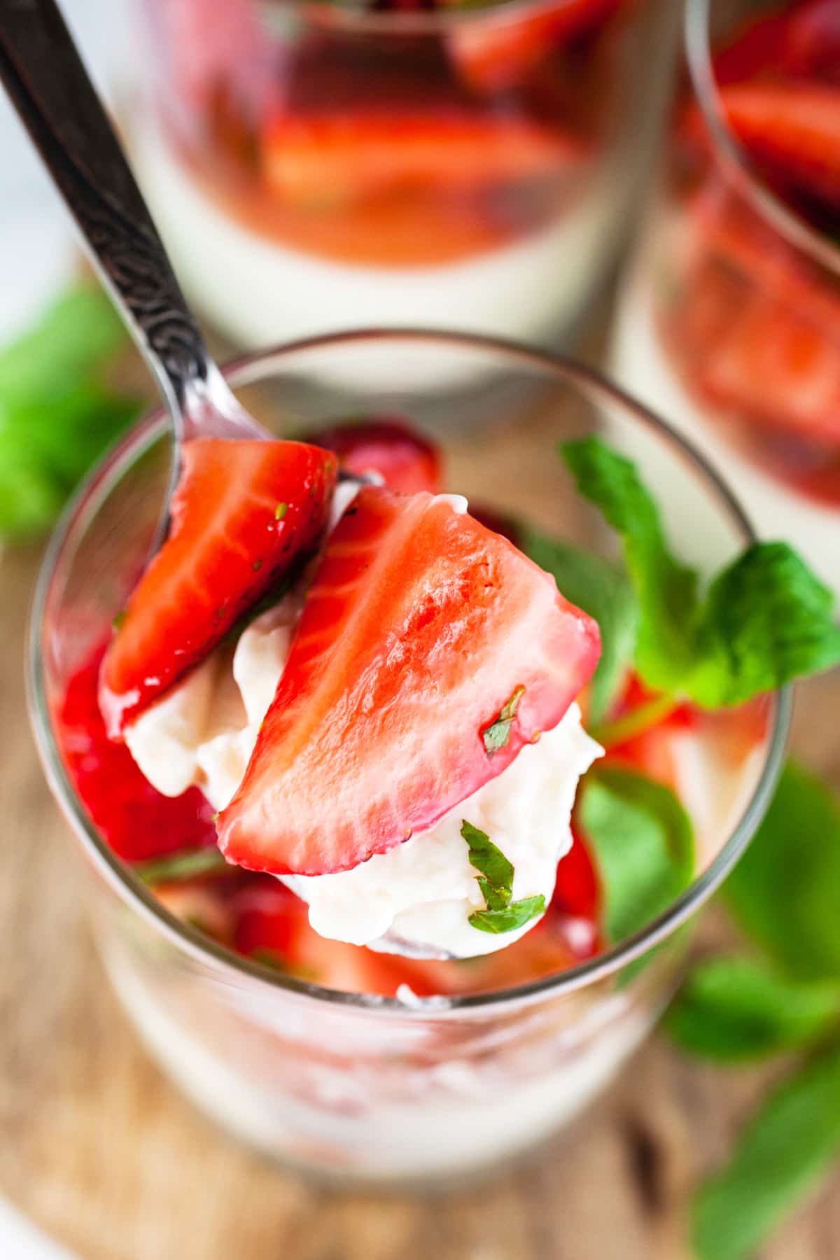 Spoonful of strawberry panna cotta lifted from glass.