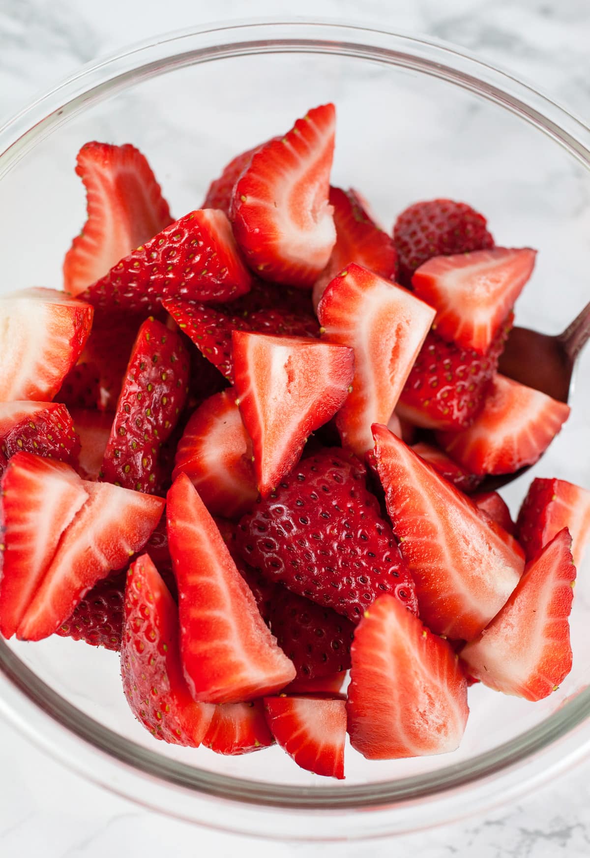 Sliced fresh strawberries in glass bowl.
