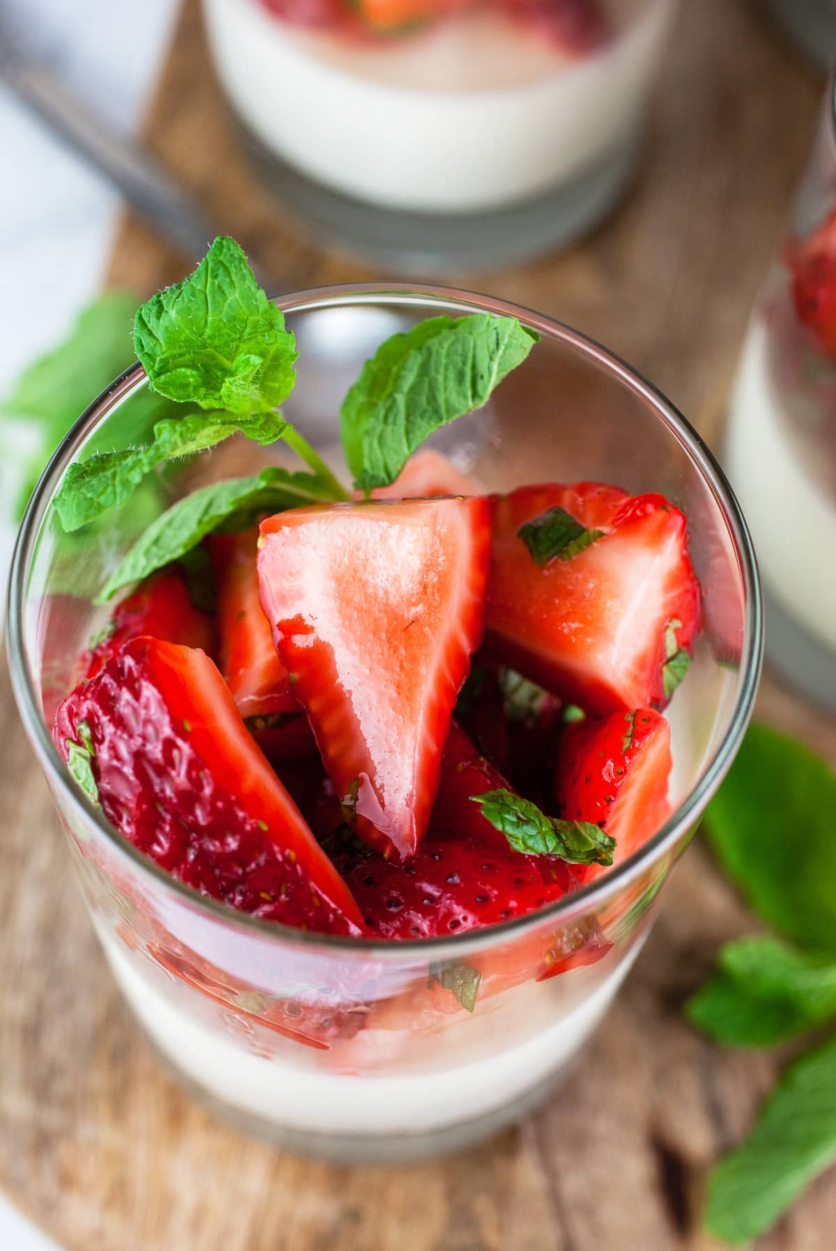 Strawberry mint panna cotta in glasses on wooden board.