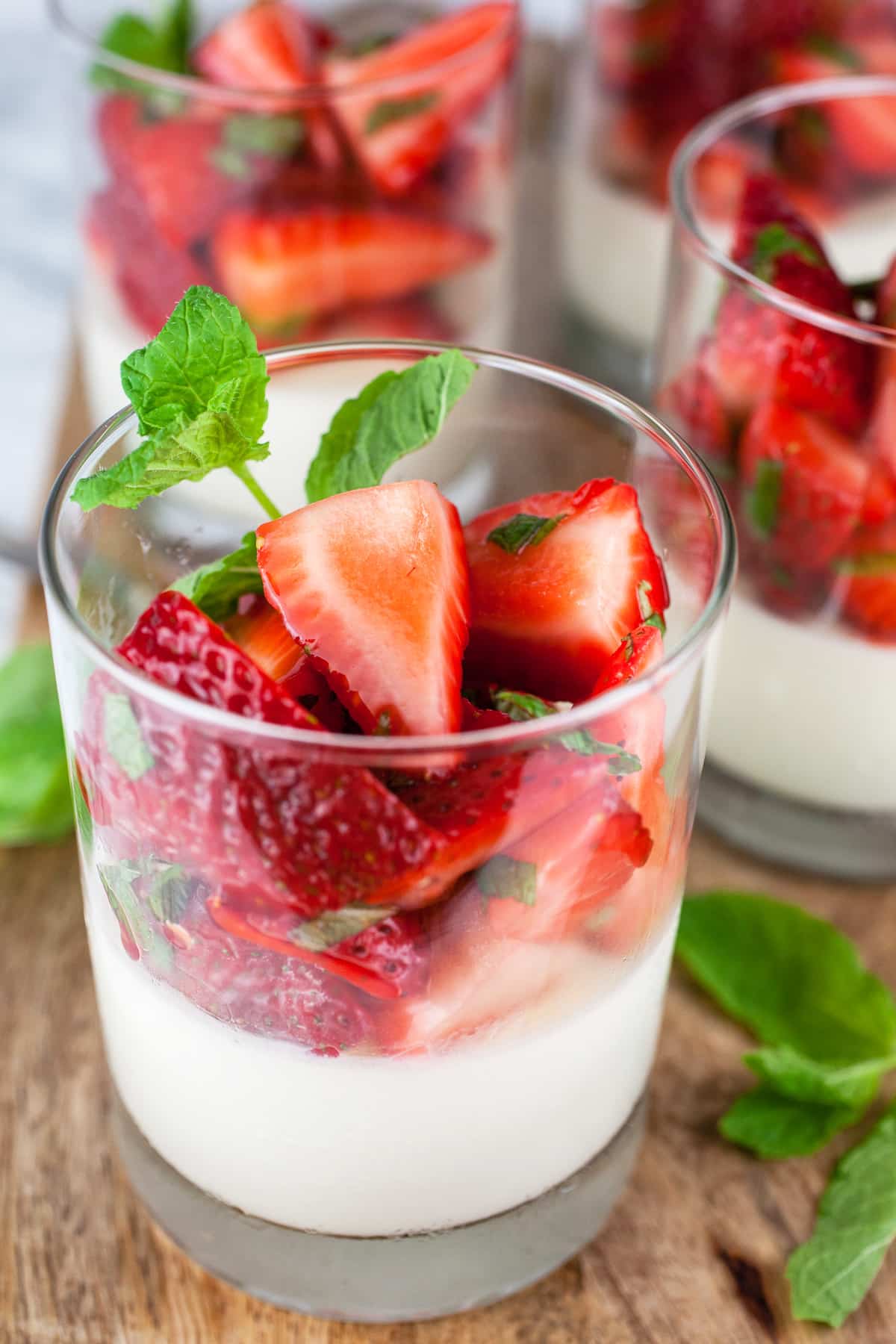 Strawberry panna cotta with fresh mint in glasses on wooden board.