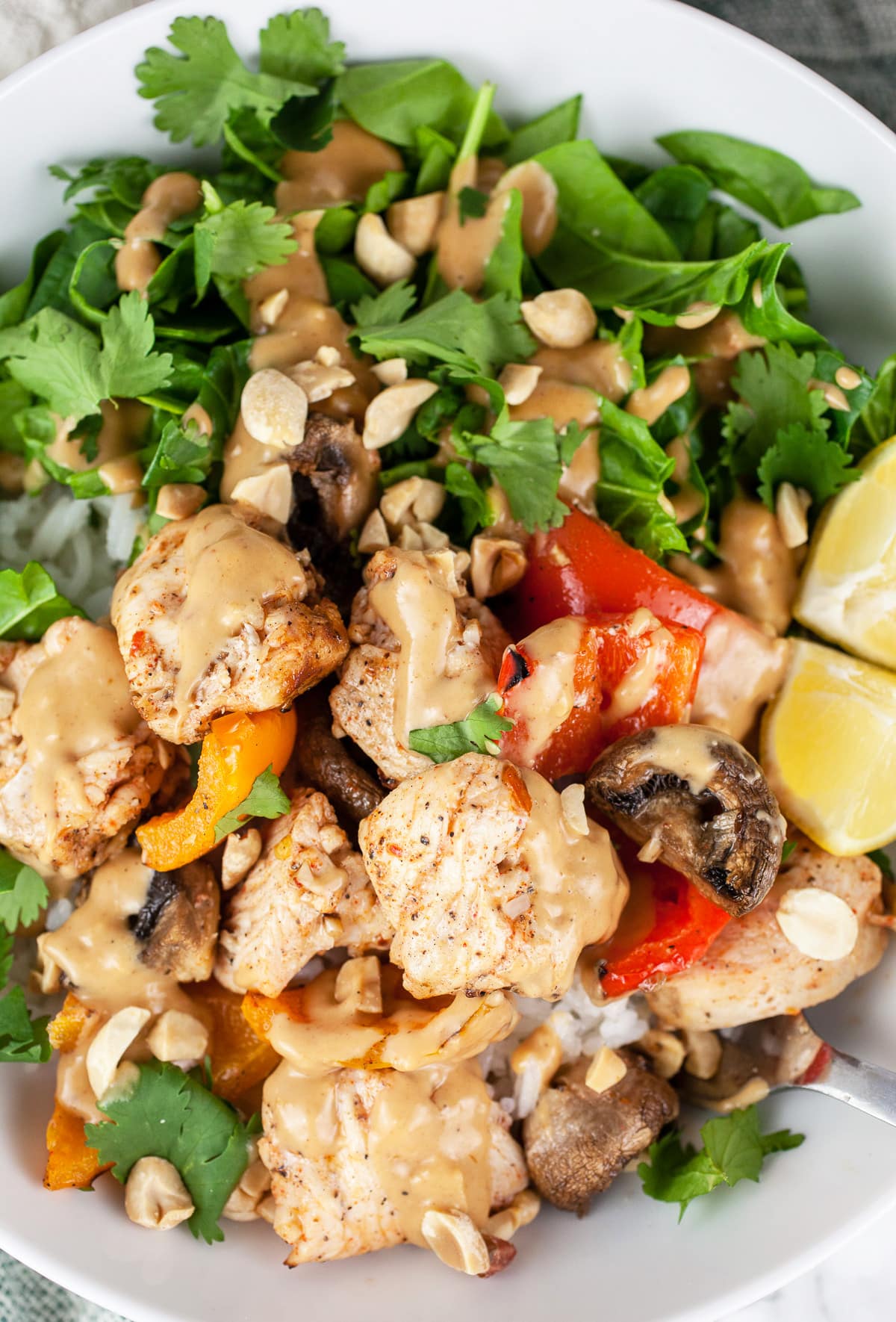 Thai chicken bowl with veggies, peanut sauce, and lemon wedges.