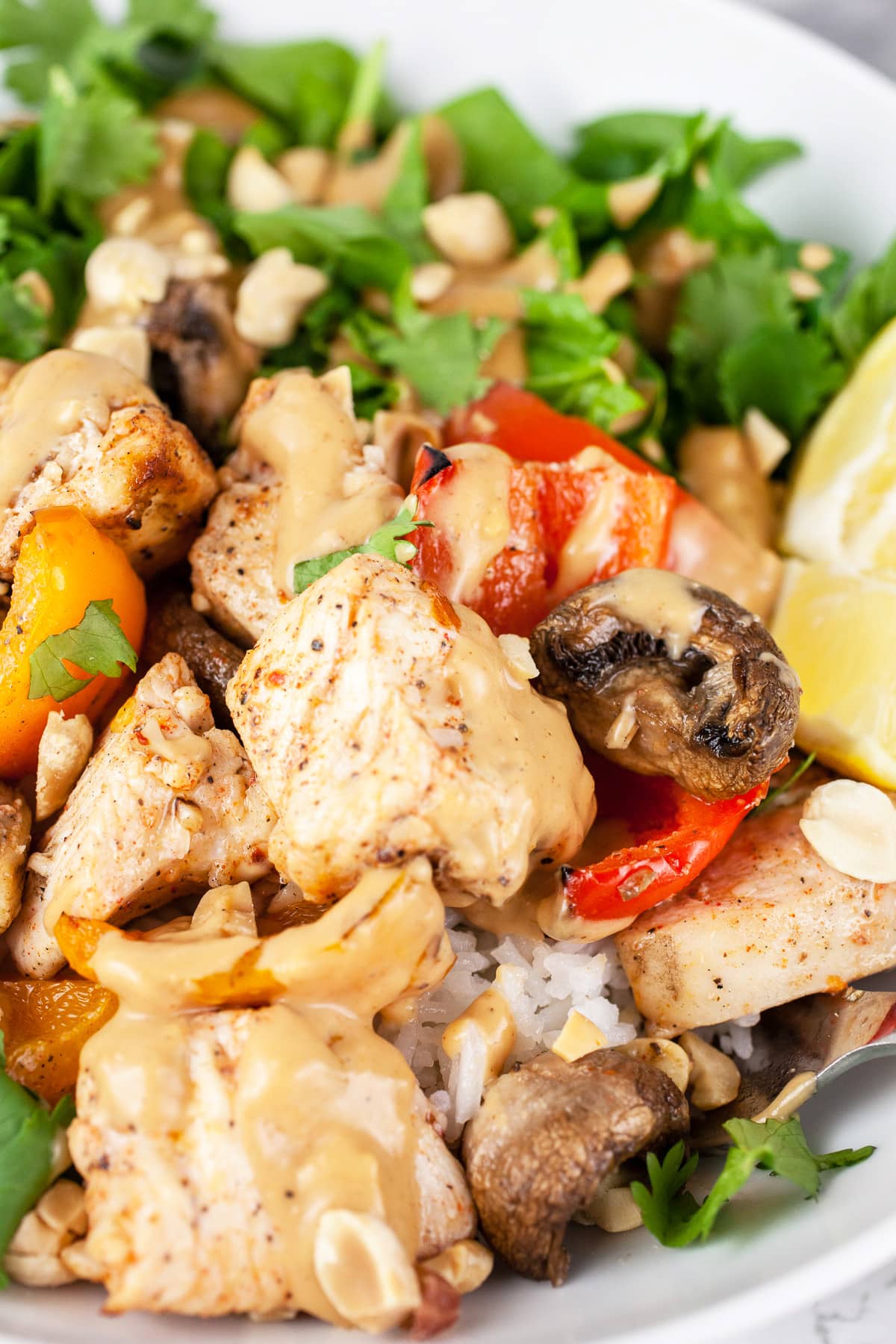 Thai chicken rice bowl with veggies, peanut sauce, and lemon wedges.