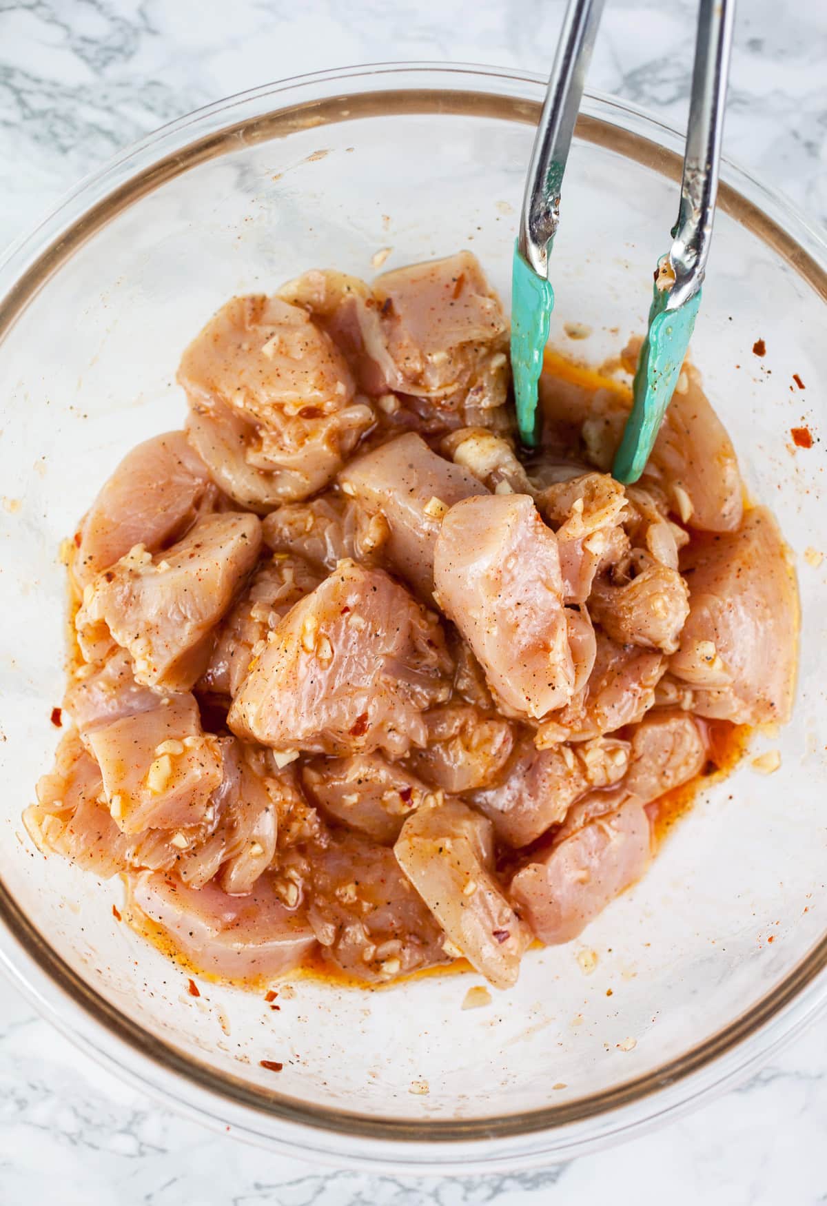Chunks of chicken marinating in large glass bowl.