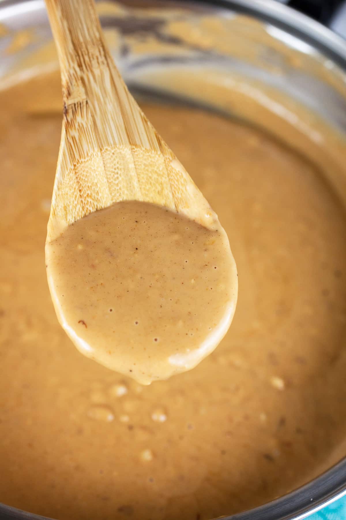 Wooden spoonful of peanut sauce lifted from skillet.