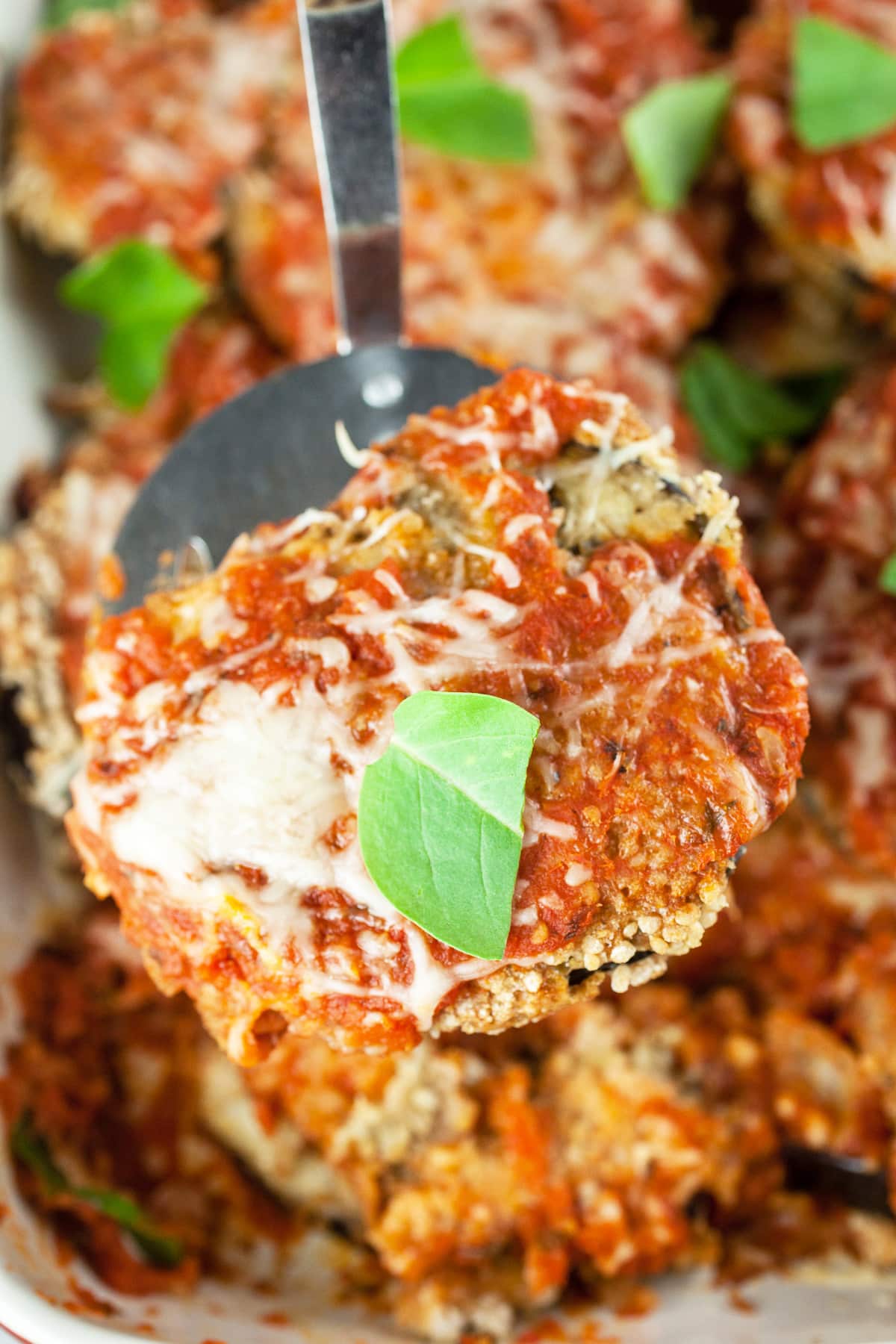 Baked eggplant parmesan slice lifted from casserole dish on metal spatula.