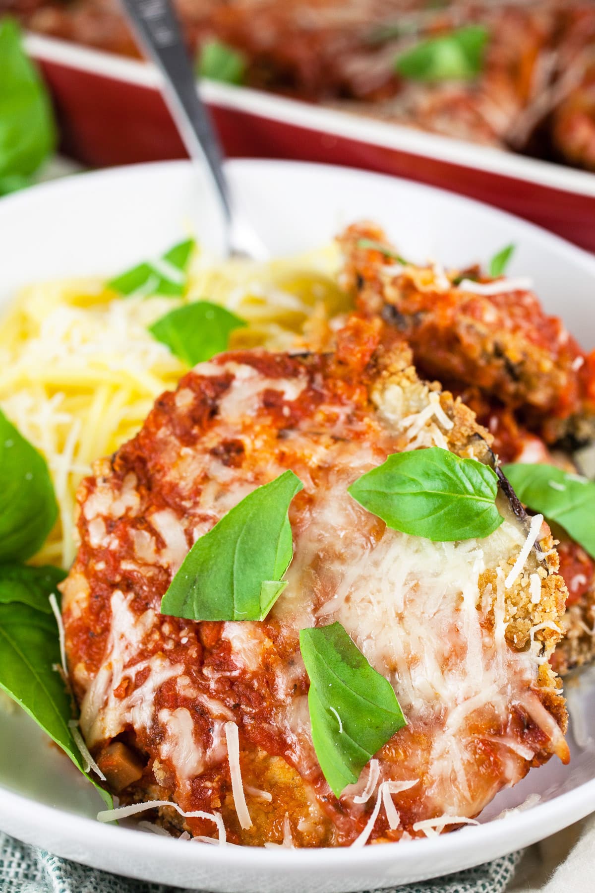Eggplant Parmesan with fresh basil and spaghetti in white bowl with fork.