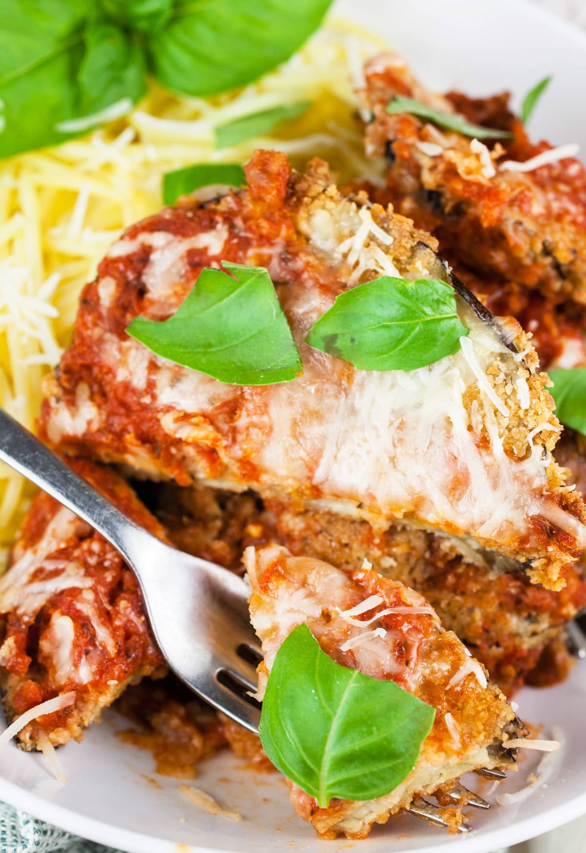 This Easy Baked Eggplant Parmesan recipe is the perfect vegetarian healthy comfort food! Eggplant slices are breaded and then baked until crispy. The eggplant is coated in marinara and Parmesan cheese then baked until hot and bubbly. Serve with pasta for a simple traditional Italian dinner. The whole family will love this classic dish! #eggplant #parmesan #vegetarian #easy #baked #healthy #italian #recipe Forkful of eggplant parmesan lifted from white bowl.