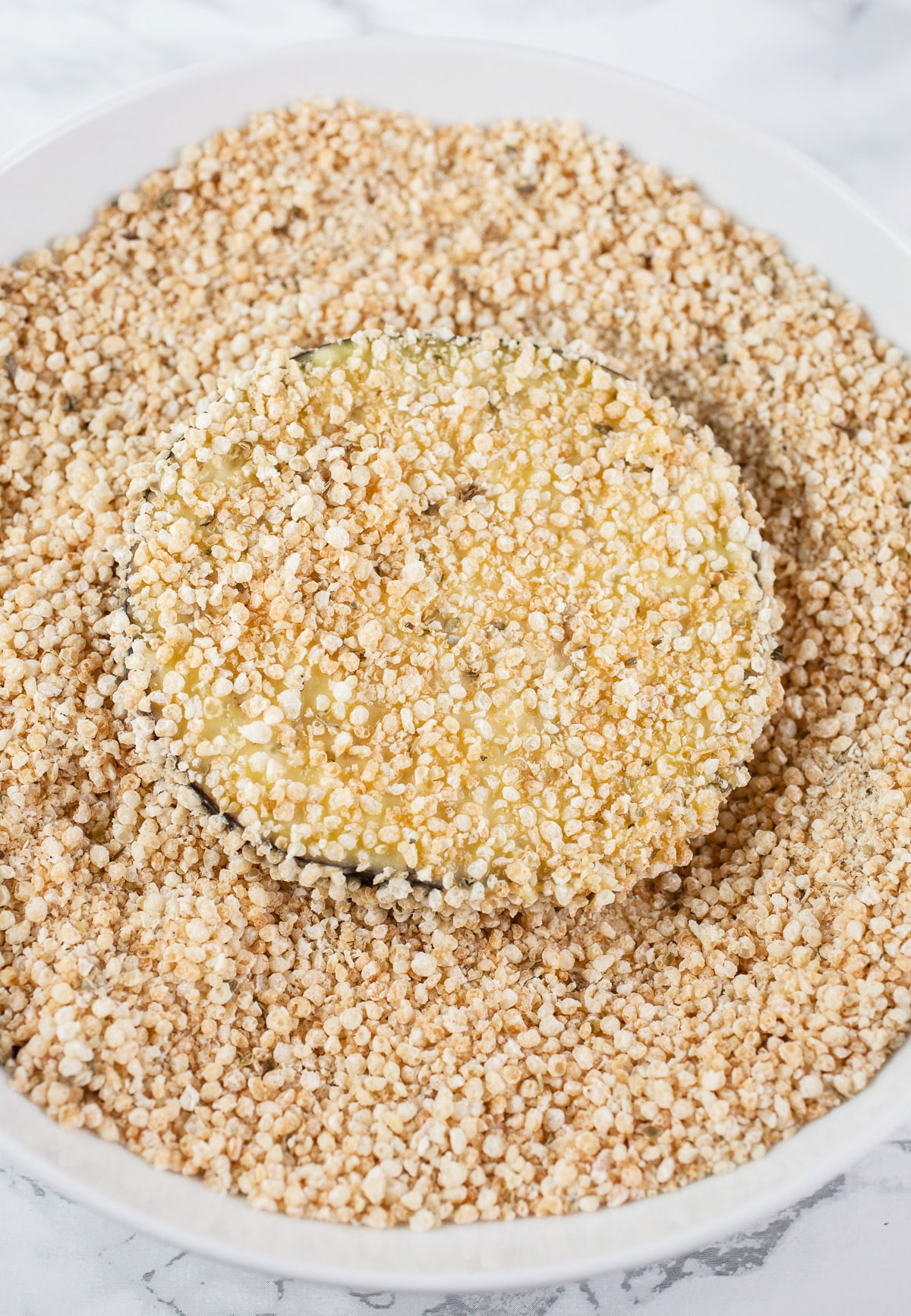 Eggplant slice coated in spiced Panko breadcrumb mixture in white bowl.