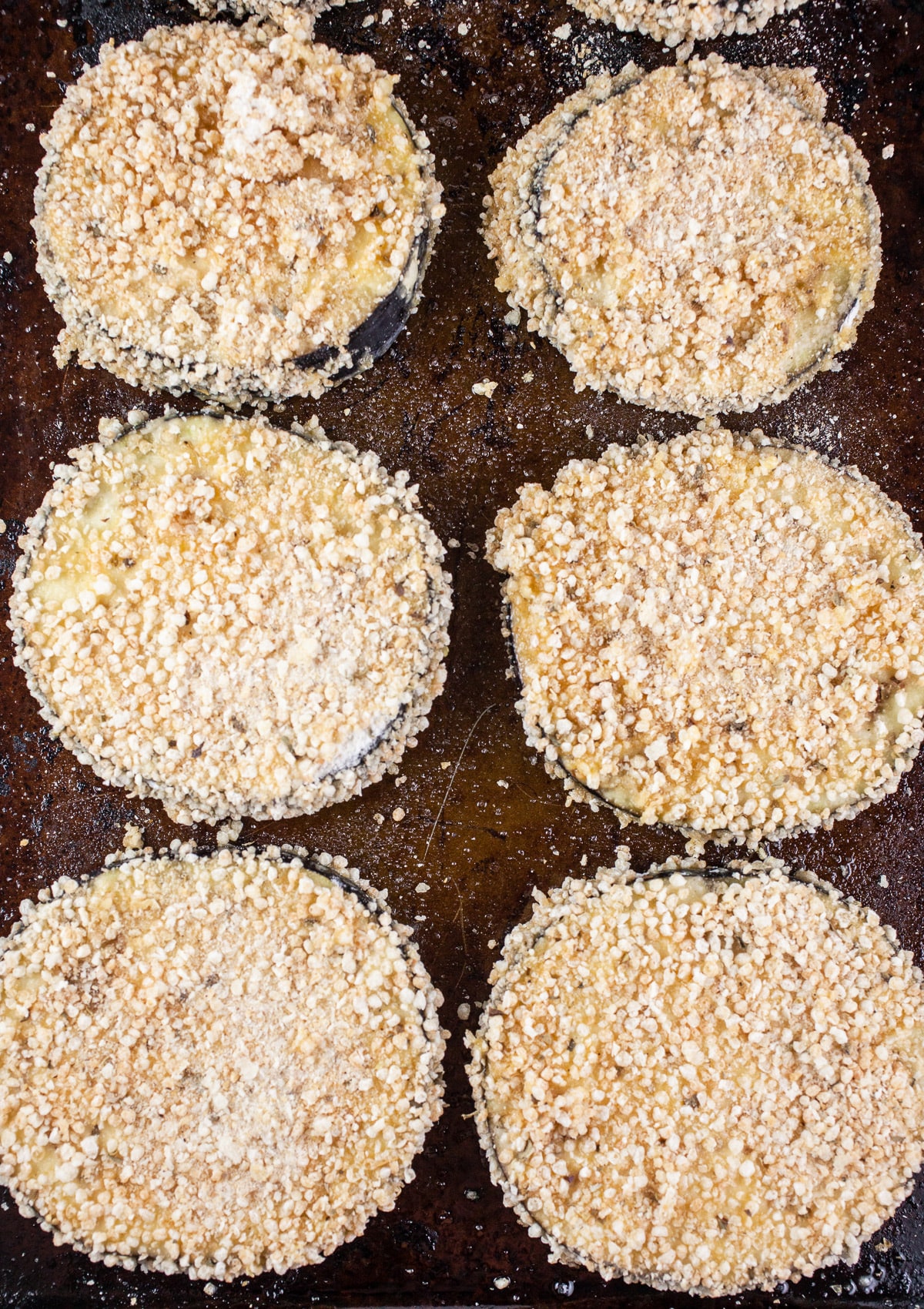Uncooked breaded eggplant slices on baking sheet.