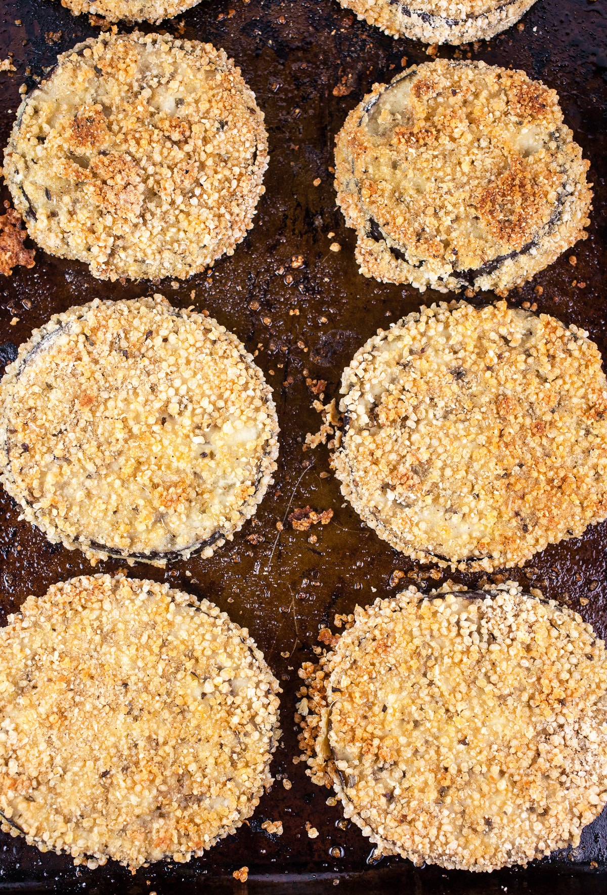 Breaded baked eggplant slices on baking sheet.