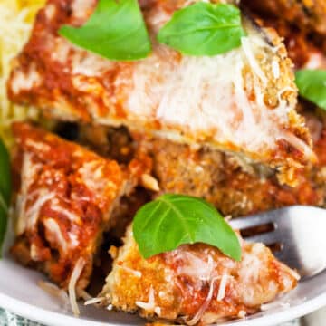 Eggplant Parmesan with basil leaves cut with fork in white bowl.