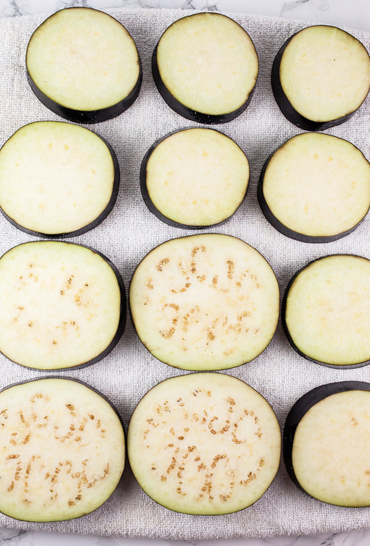 Salted eggplant slices on white towel.