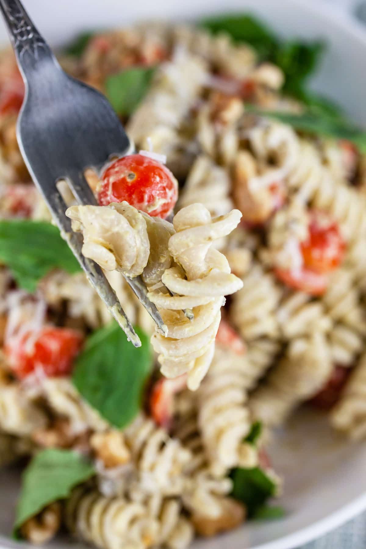 Forkful of pesto pasta salad lifted from white bowl.