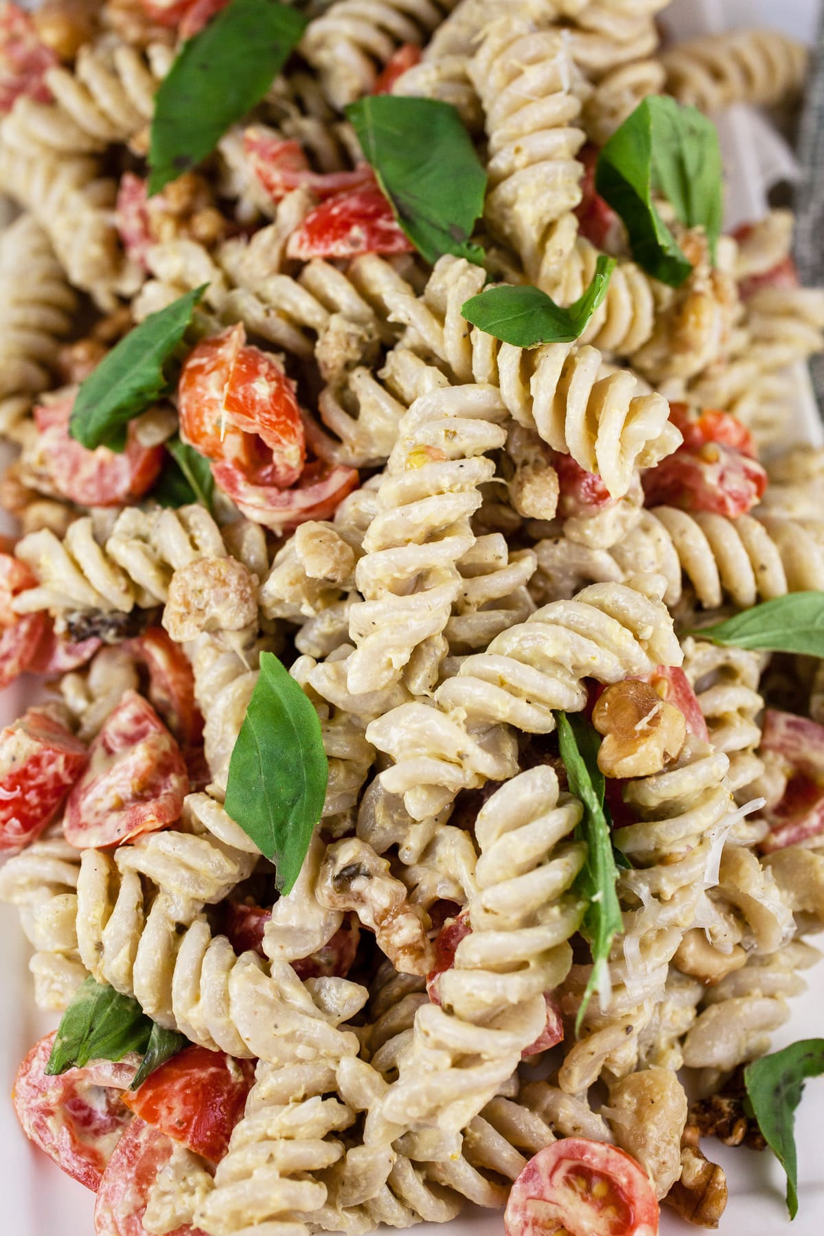 Pesto pasta salad with tomatoes, walnuts, and fresh basil on platter.