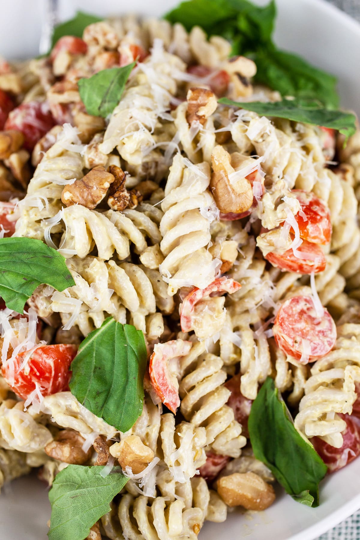 Summer pesto pasta salad with tomatoes, walnuts, and fresh basil in white bowl.