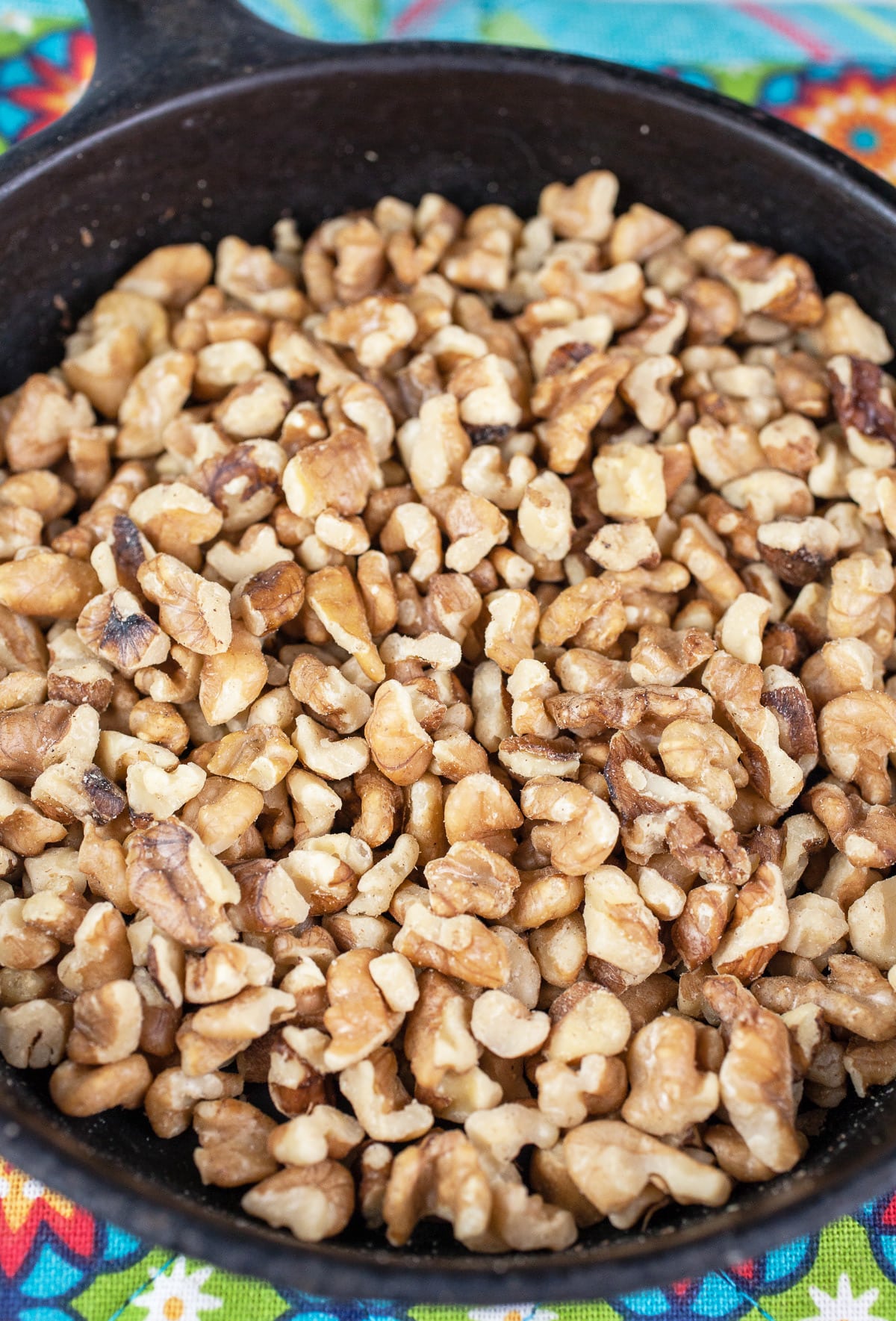 Toasted walnuts in cast iron skillet on colorful potholder.