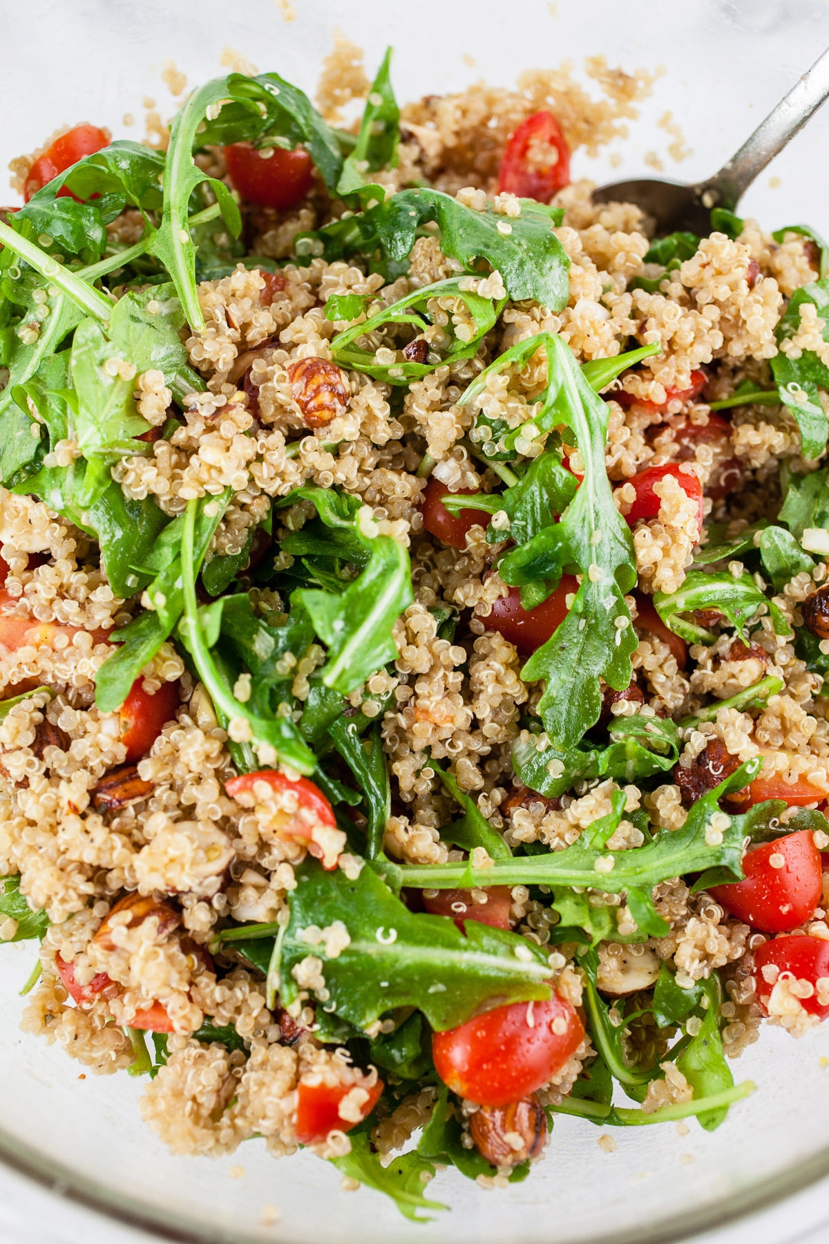 Quinoa salad tossed in large glass bowl with spoon.