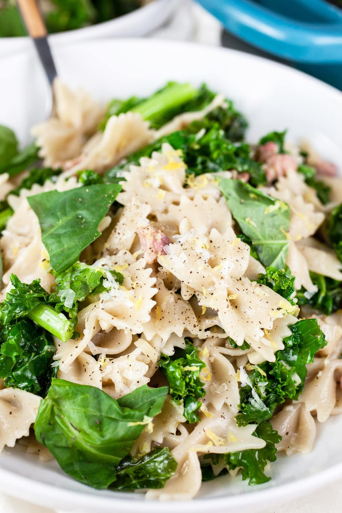 Kale pancetta pasta in white bowl with fork.
