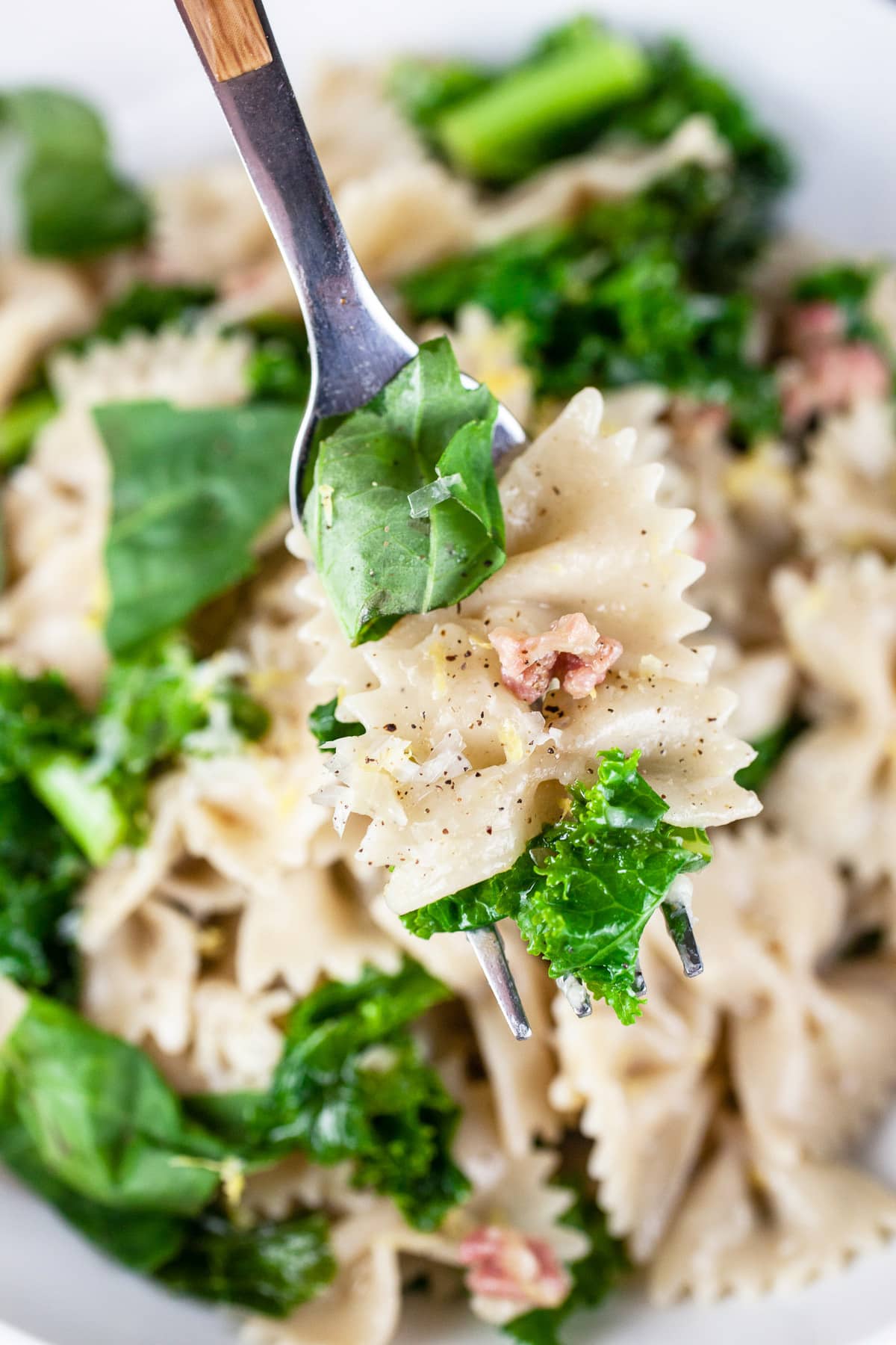 Forkful of kale pancetta pasta lifted from white bowl.