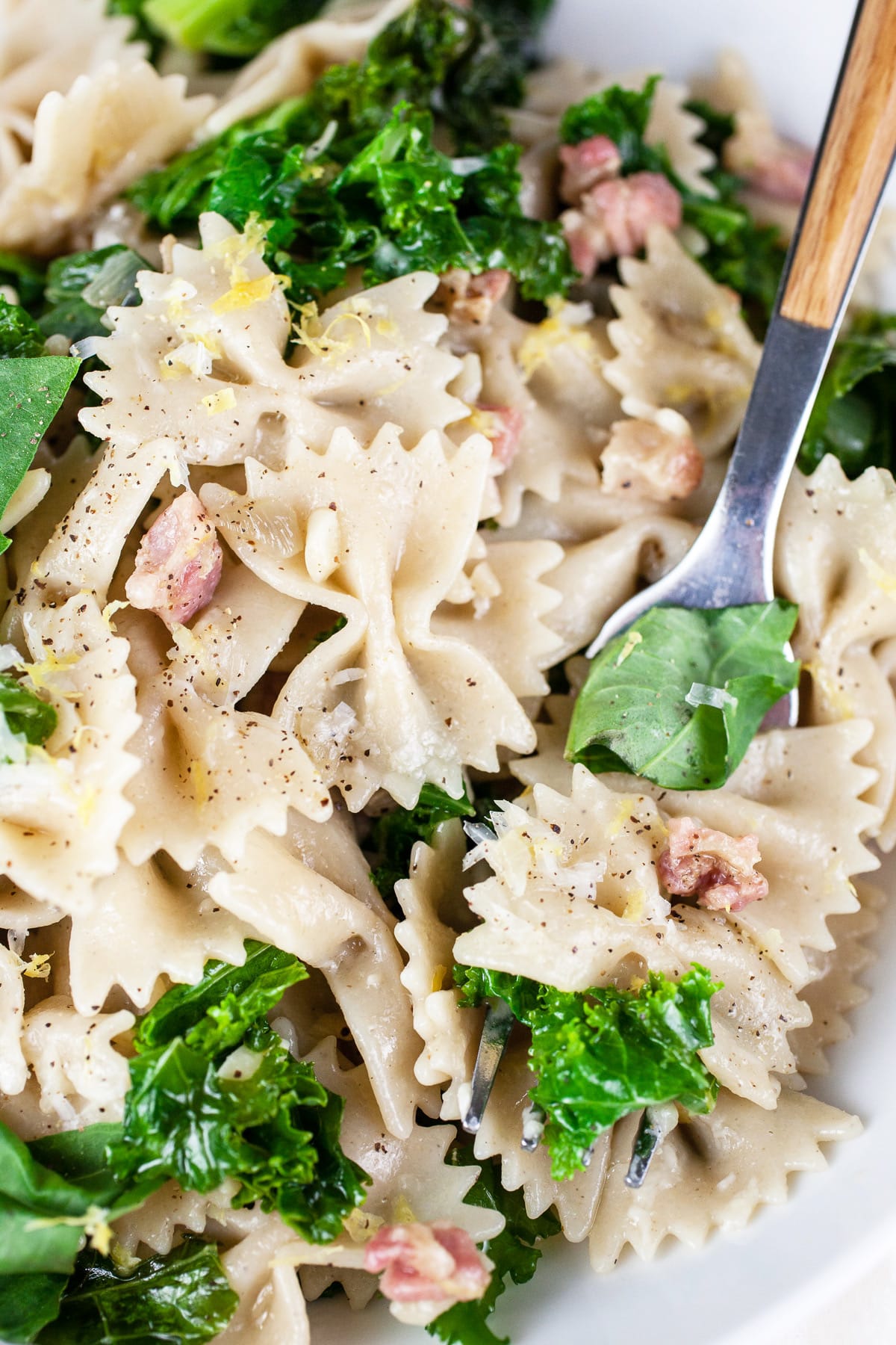 Kale pancetta pasta in white bowl with fork.