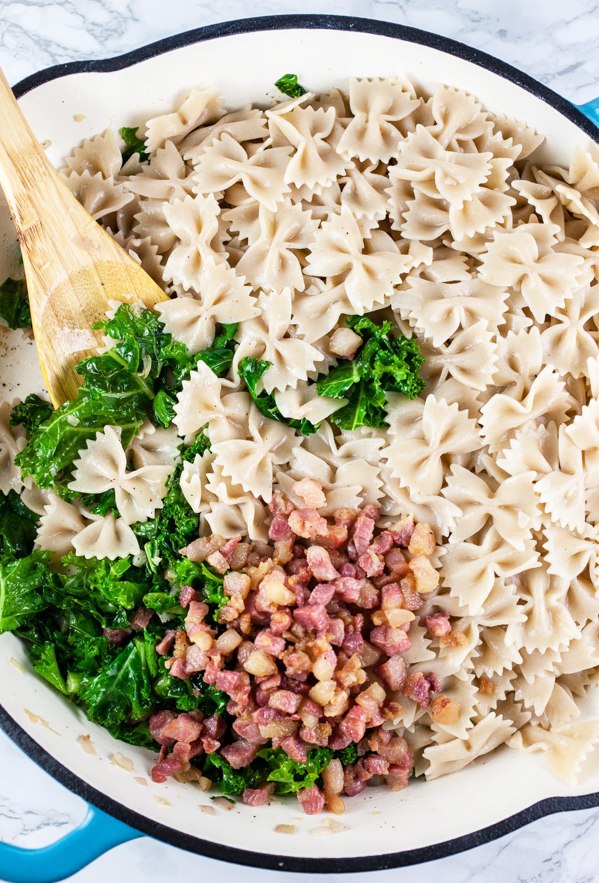 Cooked farfalle pasta, pancetta, and kale in skillet.