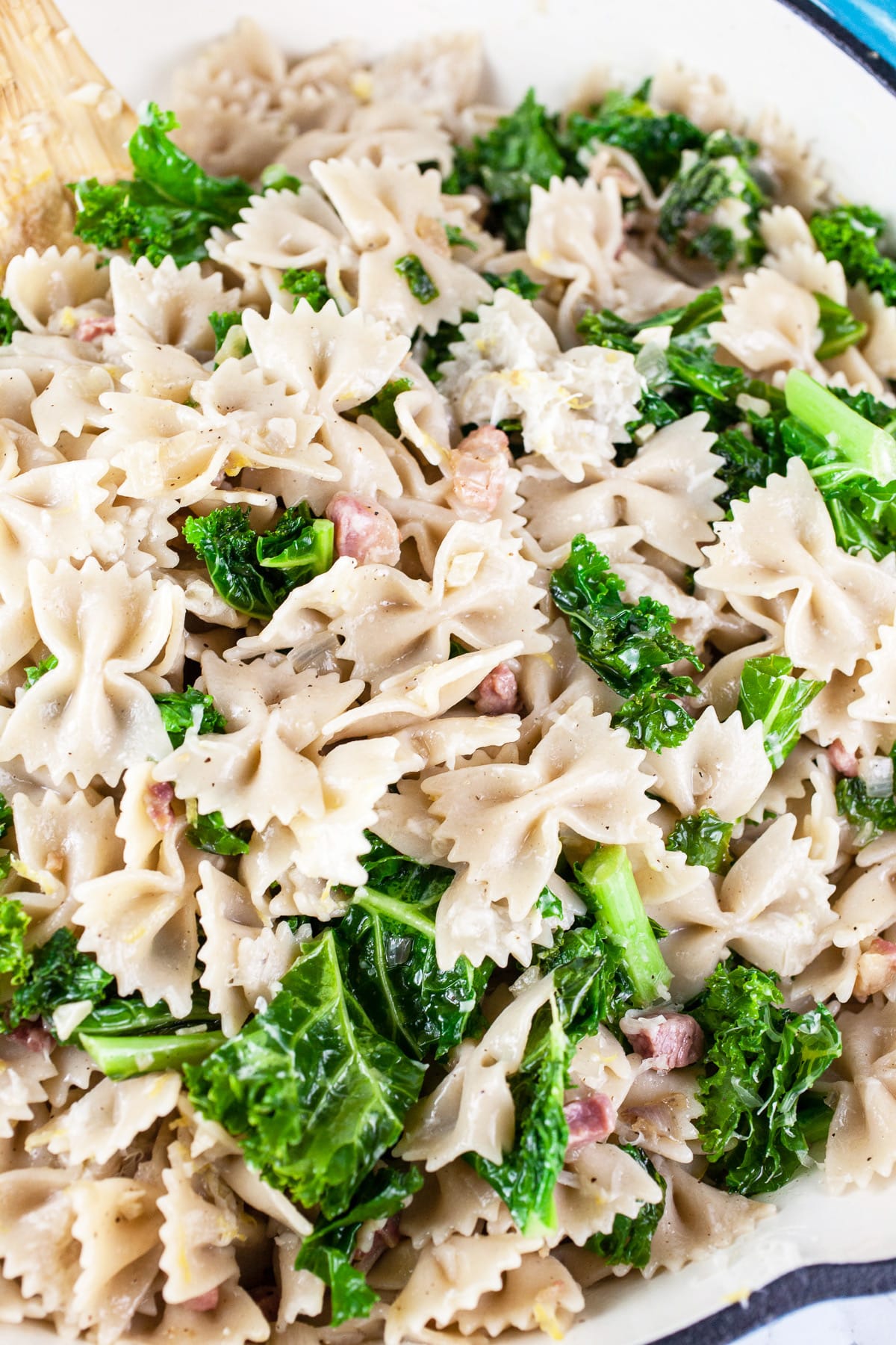 Pancetta kale pasta in skillet with wooden spoon.