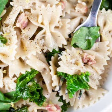 Kale pancetta pasta in white bowl with fork.