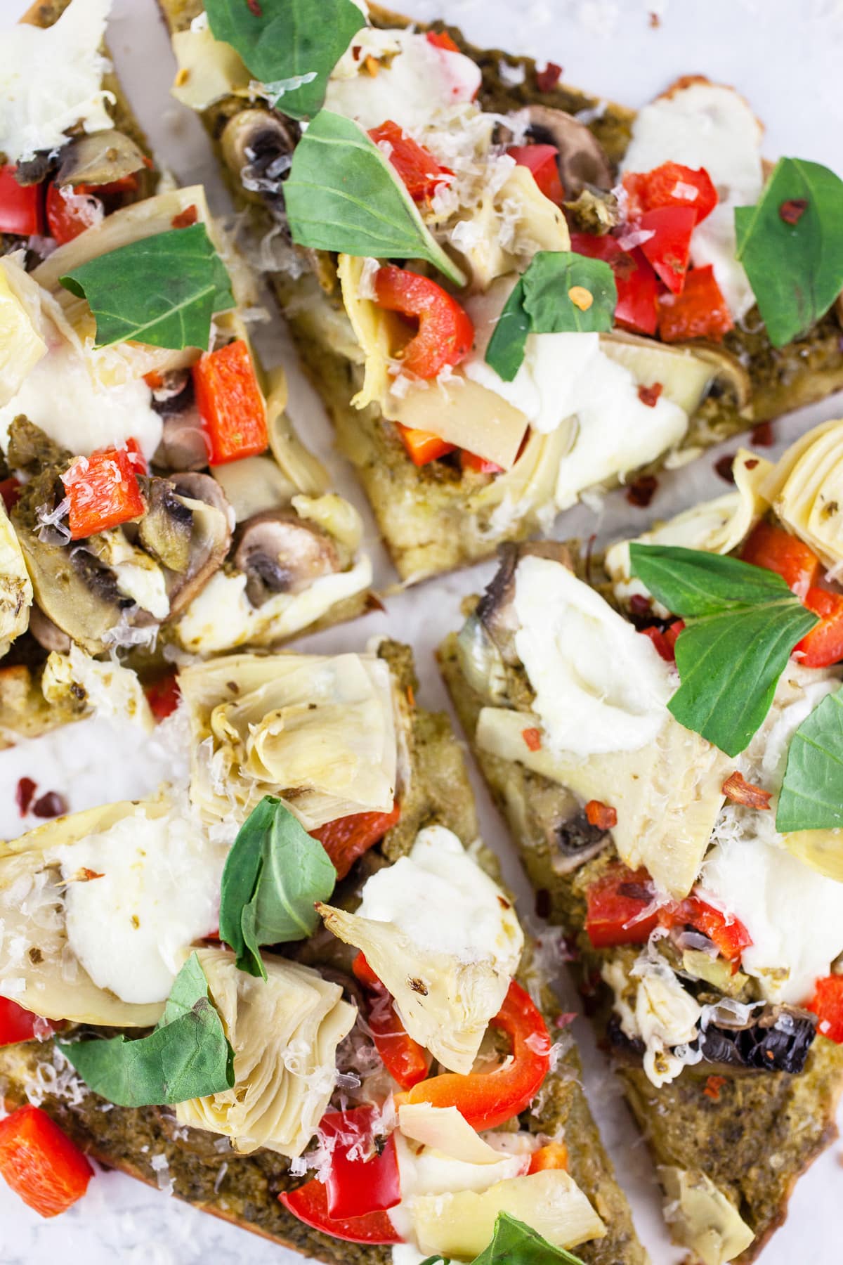 Mediterranean veggie flatbread pizza with fresh basil cut into slices.