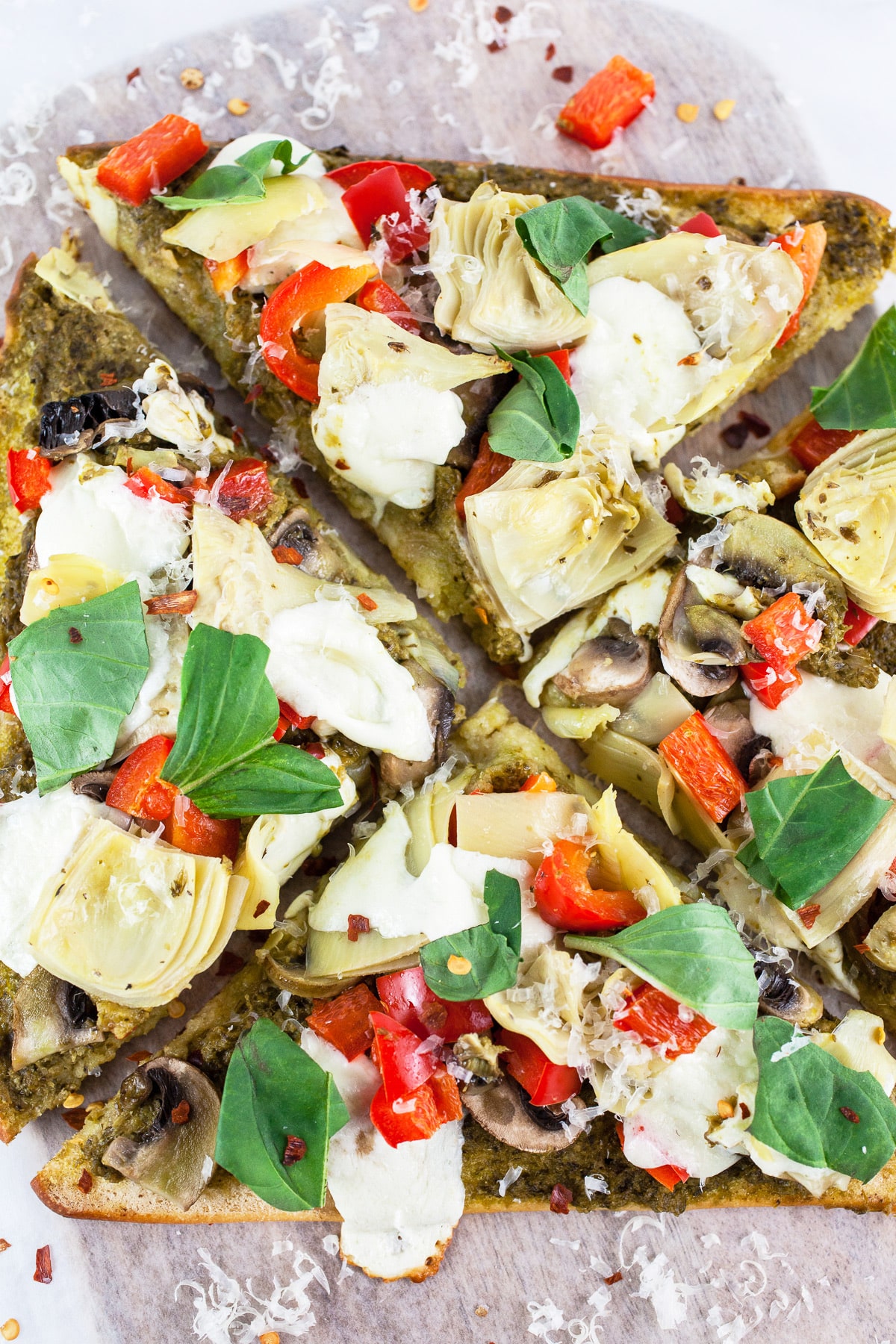 Mediterranean veggie flatbread pizza cut into slices with fresh basil.