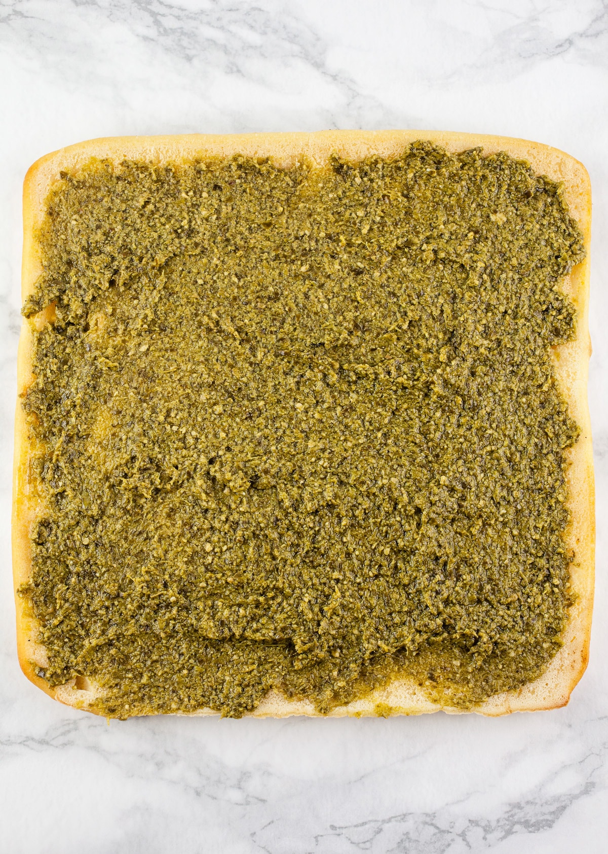 Basil pesto spread on uncooked flatbread.