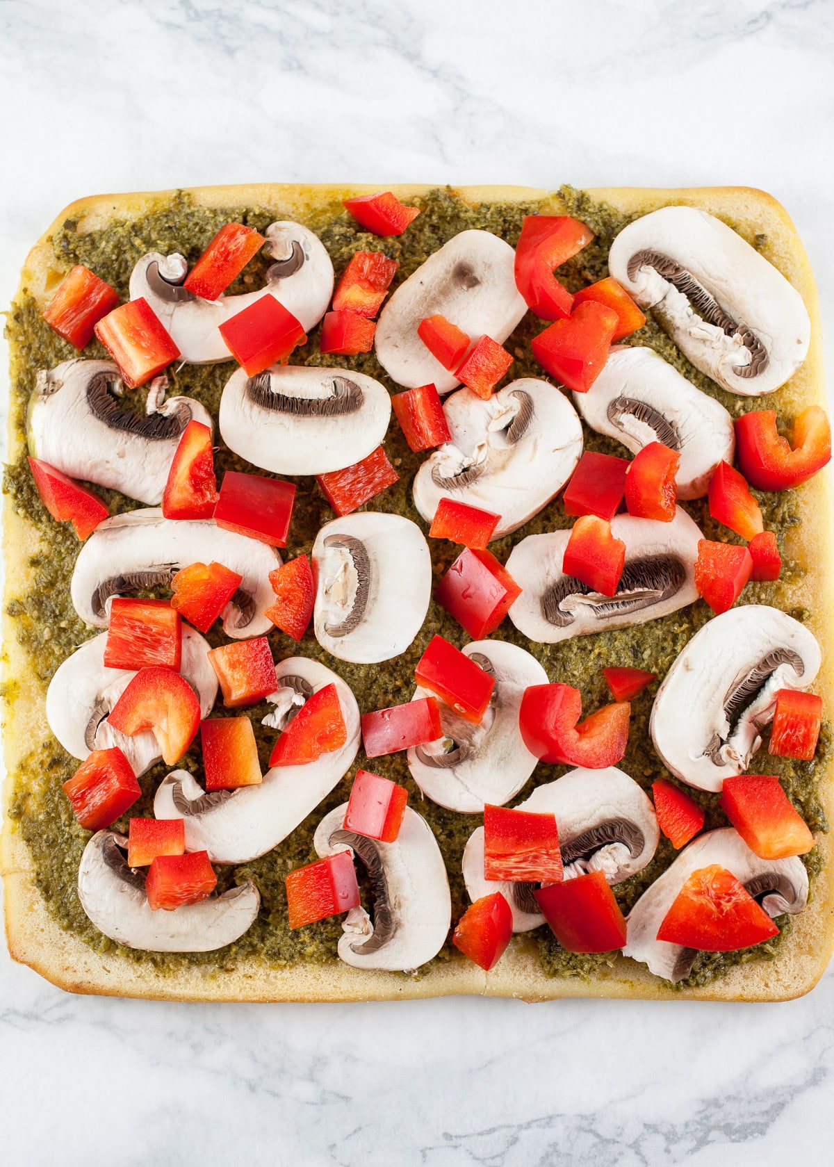 Pesto, red bell peppers, and mushrooms on uncooked flatbread.