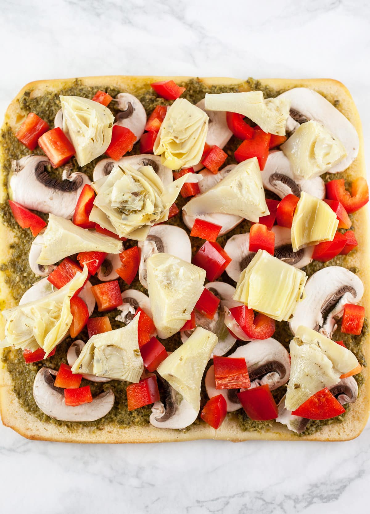 Pesto, red bell peppers, mushrooms, and artichokes on uncooked flatbread.