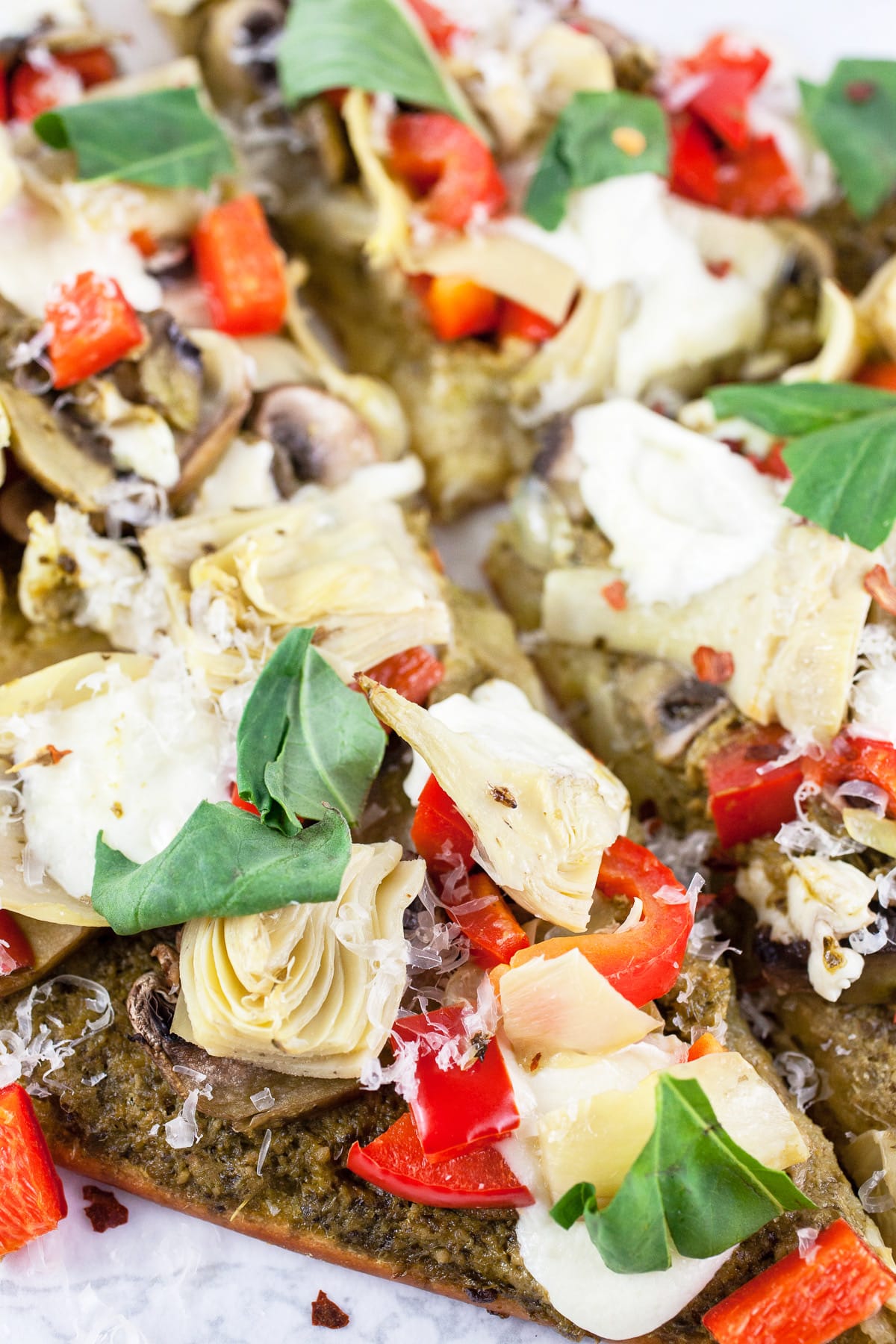 Mediterranean veggie flatbread pizza with fresh basil cut into slices.