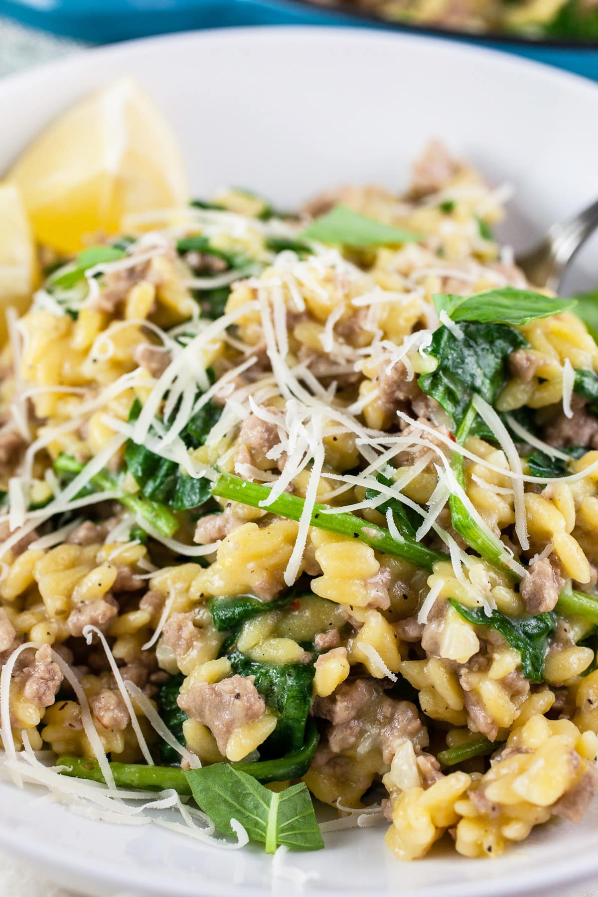 Ground turkey spinach pasta with Parmesan cheese and lemon wedges in white bowl.