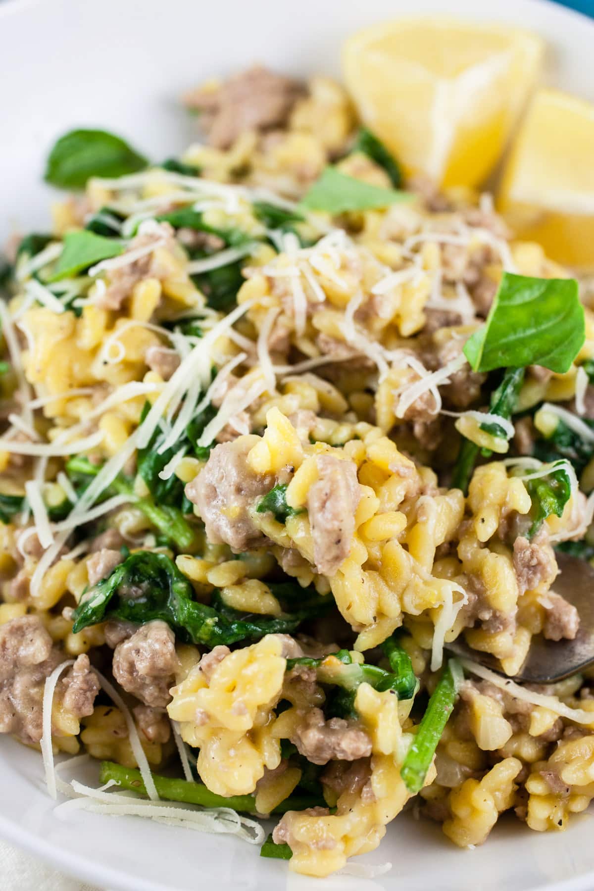 Turkey spinach pasta with Parmesan cheese and lemon wedges in white bowl.