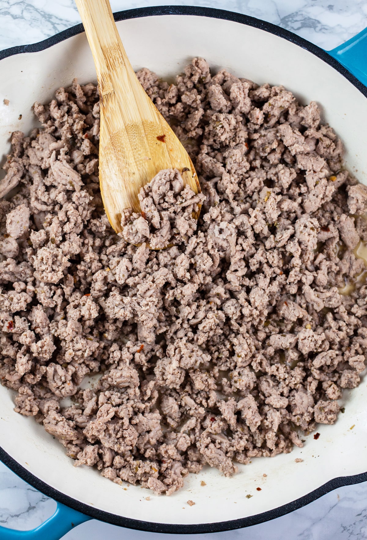 Cooked ground turkey in skillet with wooden spoon.