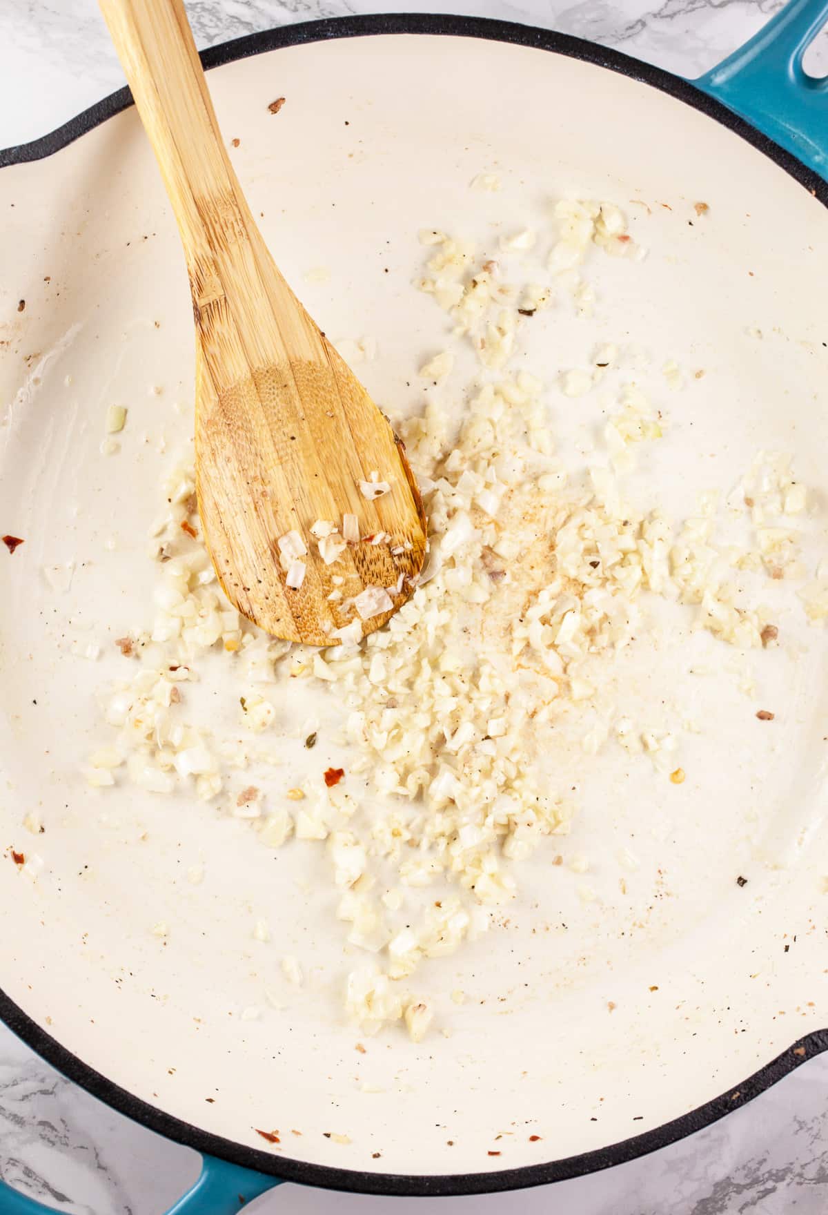 Garlic and shallots sautéed in skillet with wooden spoon.