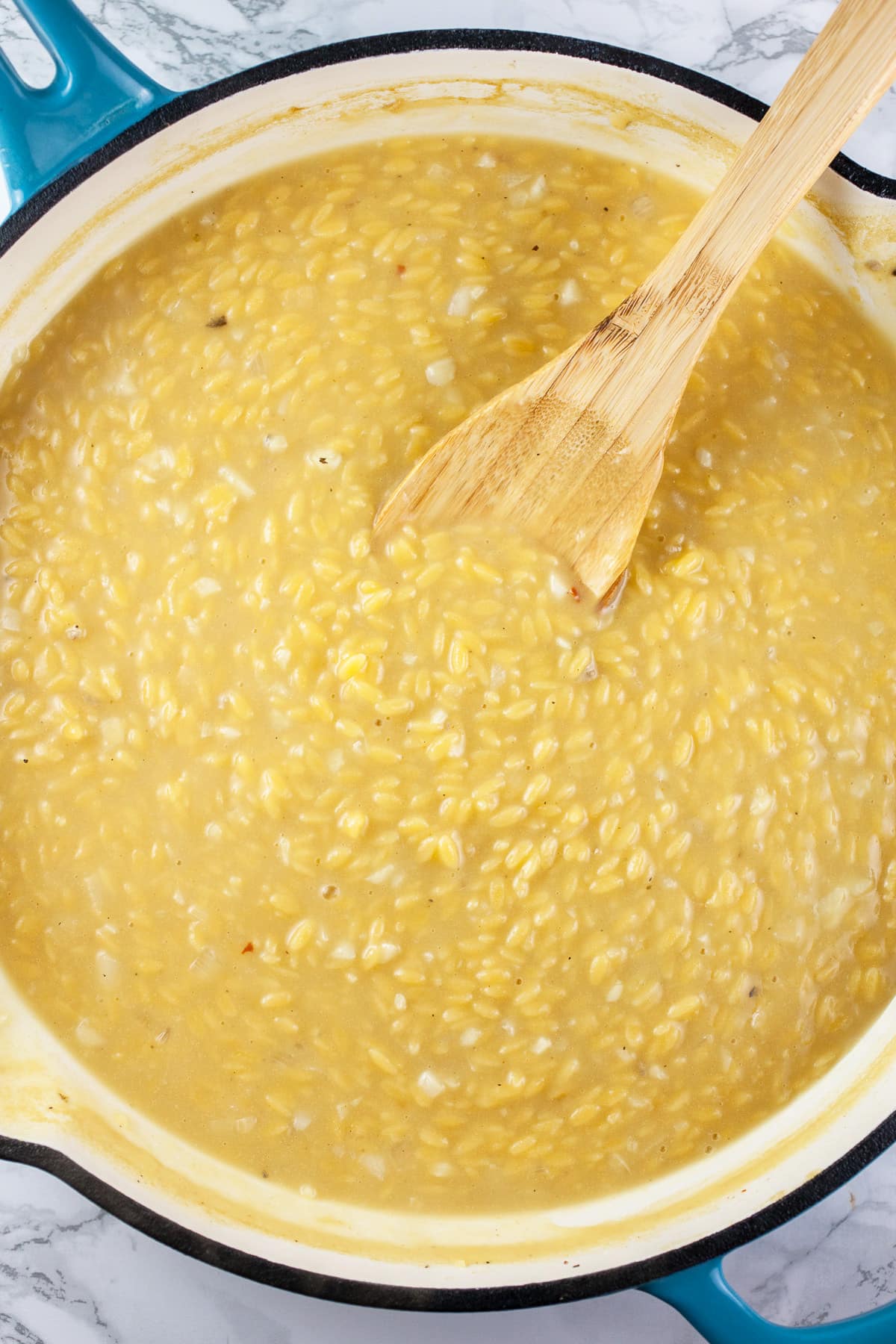 Cooked orzo pasta in broth in large skillet with wooden spoon.