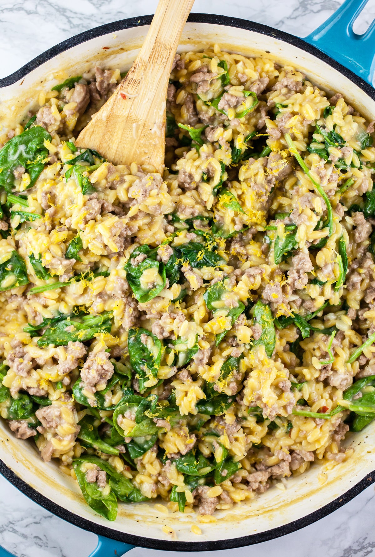 Ground turkey orzo pasta in large skillet with wooden spoon.