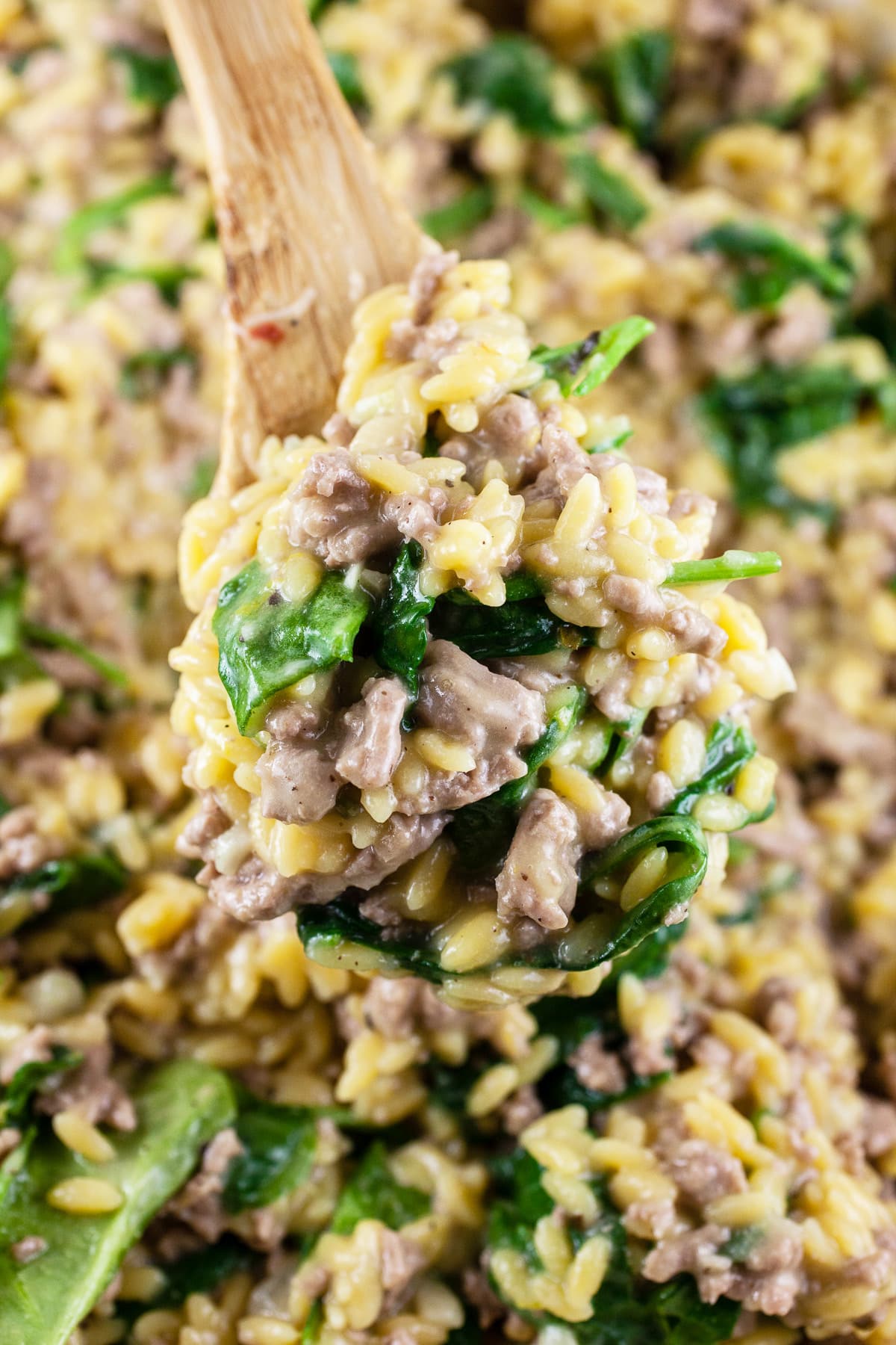 Wooden spoonful of ground turkey spinach pasta lifted from skillet.