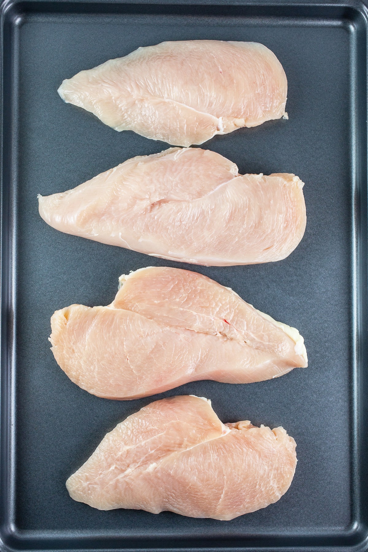 Raw chicken breasts on baking sheet.