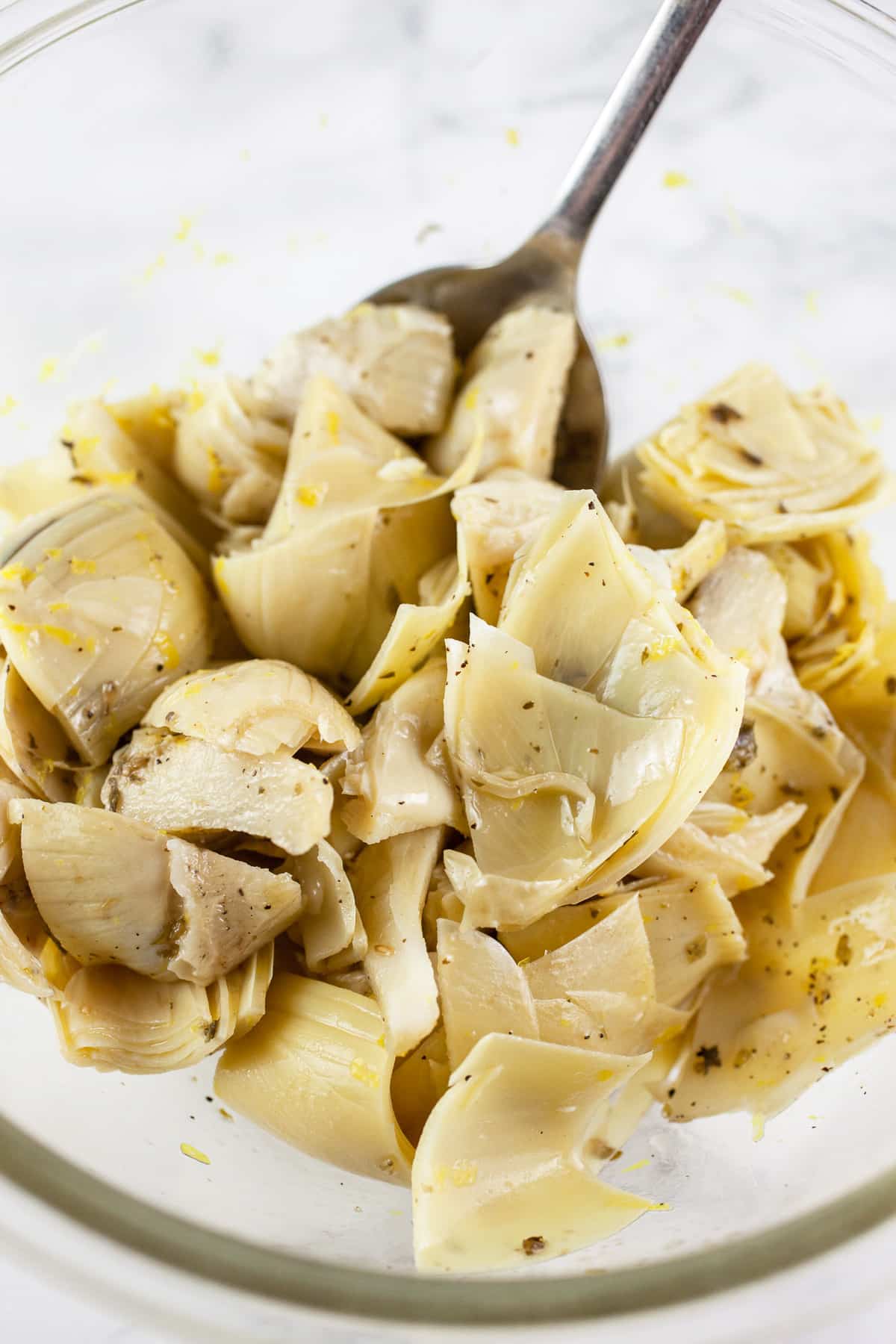 Marinated artichokes and lemon zest in small glass bowl with spoon.