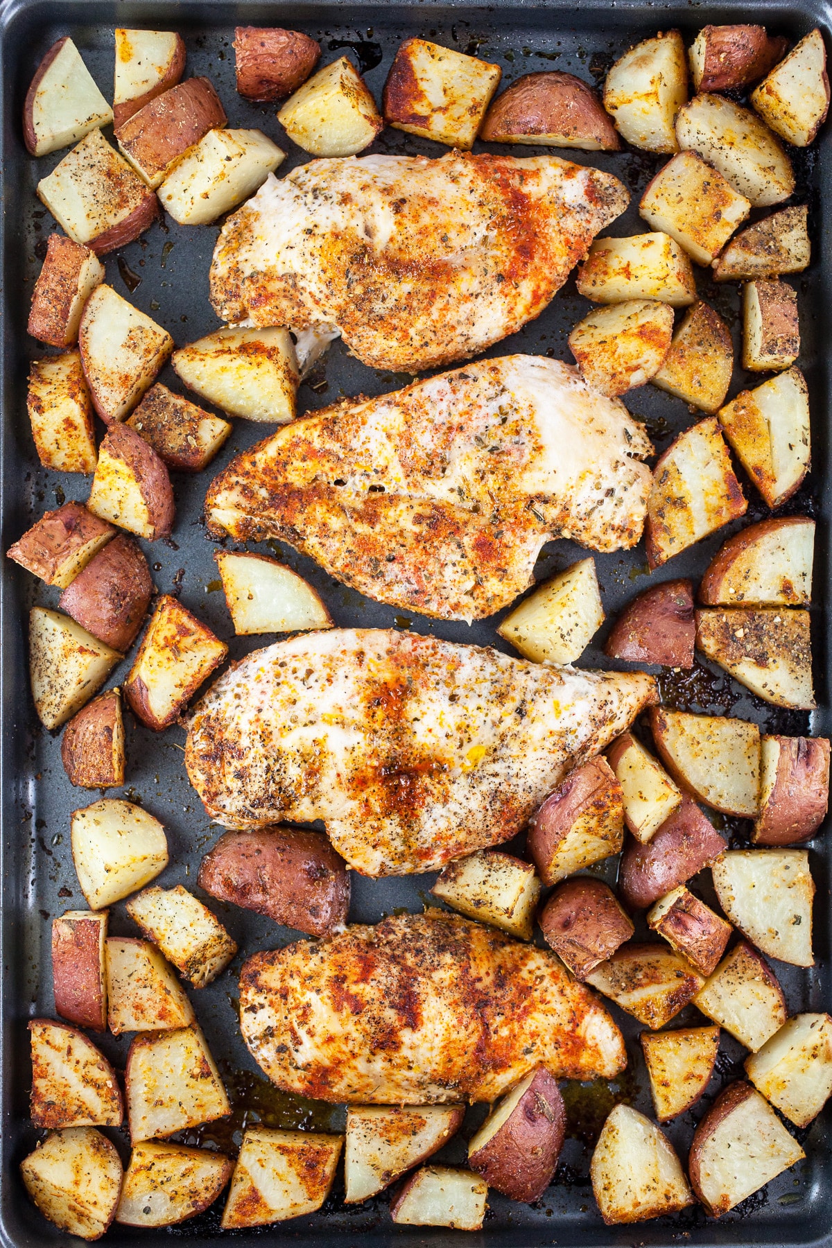 Cooked chicken and potatoes on baking sheet.