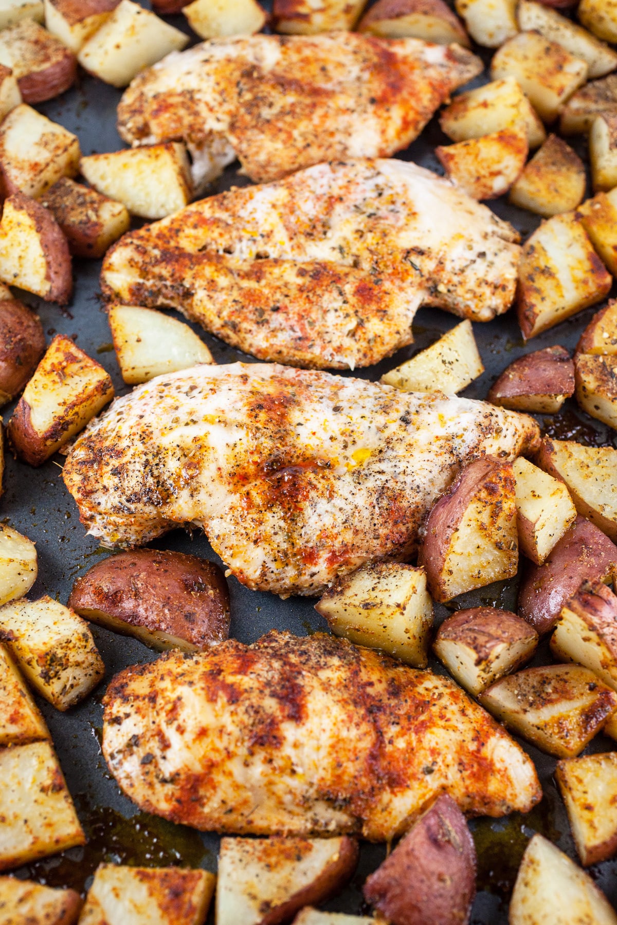 Cooked chicken breasts and potatoes on baking sheet.