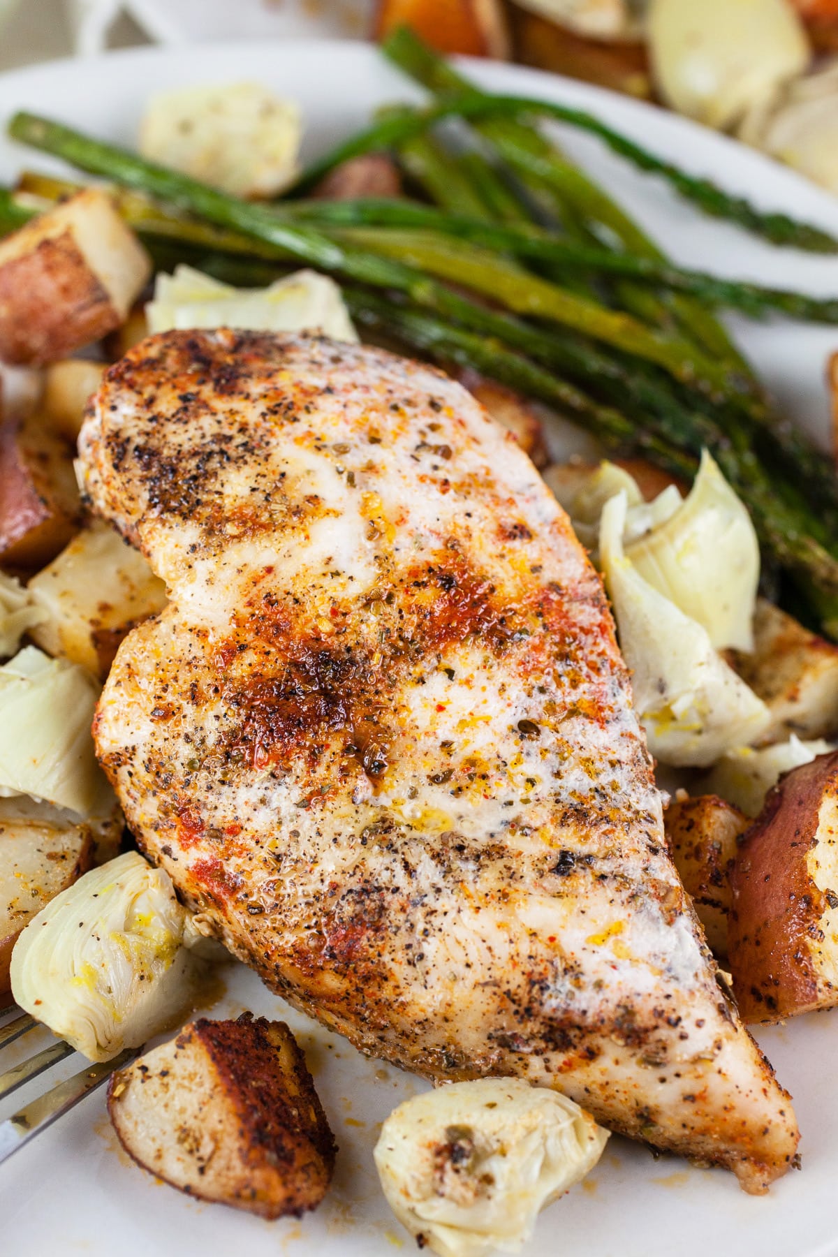 Chicken breast with roasted potatoes, asparagus, and artichokes on white plate.