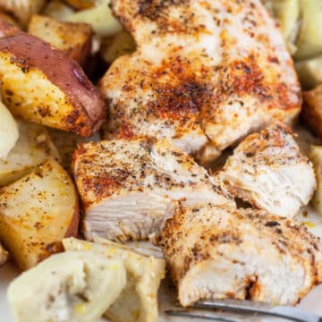 Sheet pan Mediterranean chicken and potatoes with artichokes on white plate.