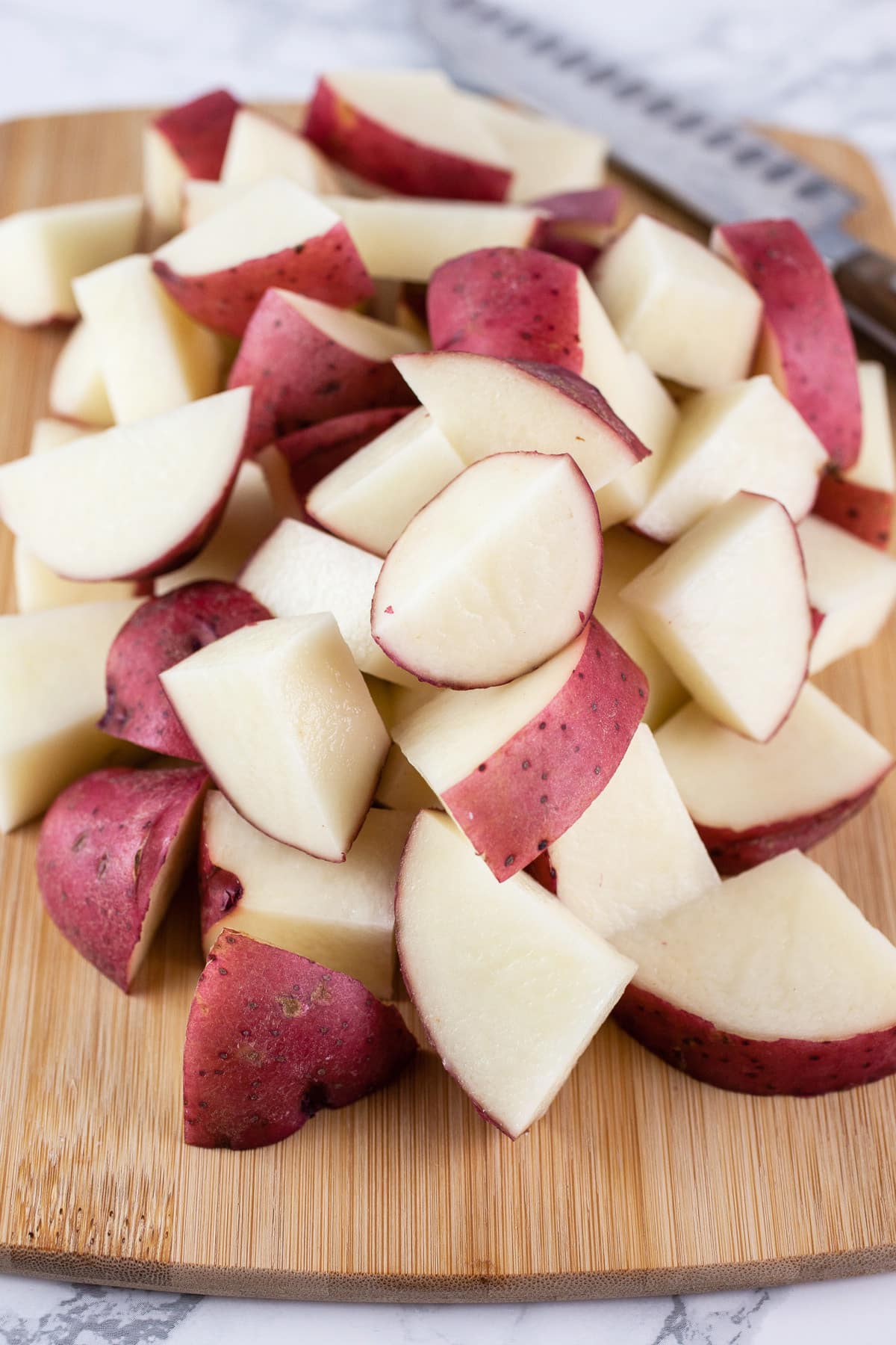 Diced red potatoes on wooden cutting board with knife.